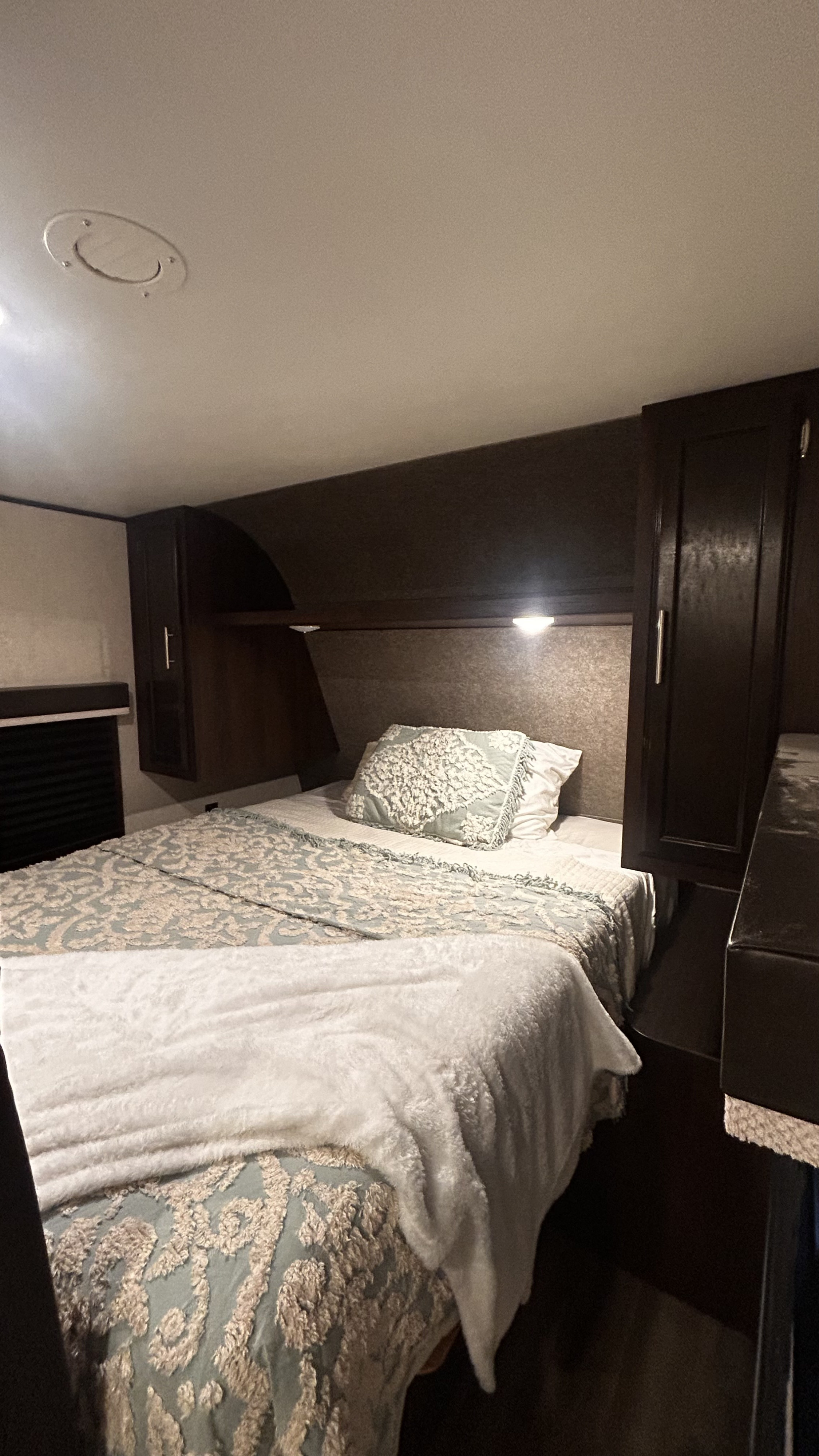 Cozy RV rental bedroom with patterned bedding, dark wood cabinets, and overhead lighting,. Jayco Jay Flight SLX 2019