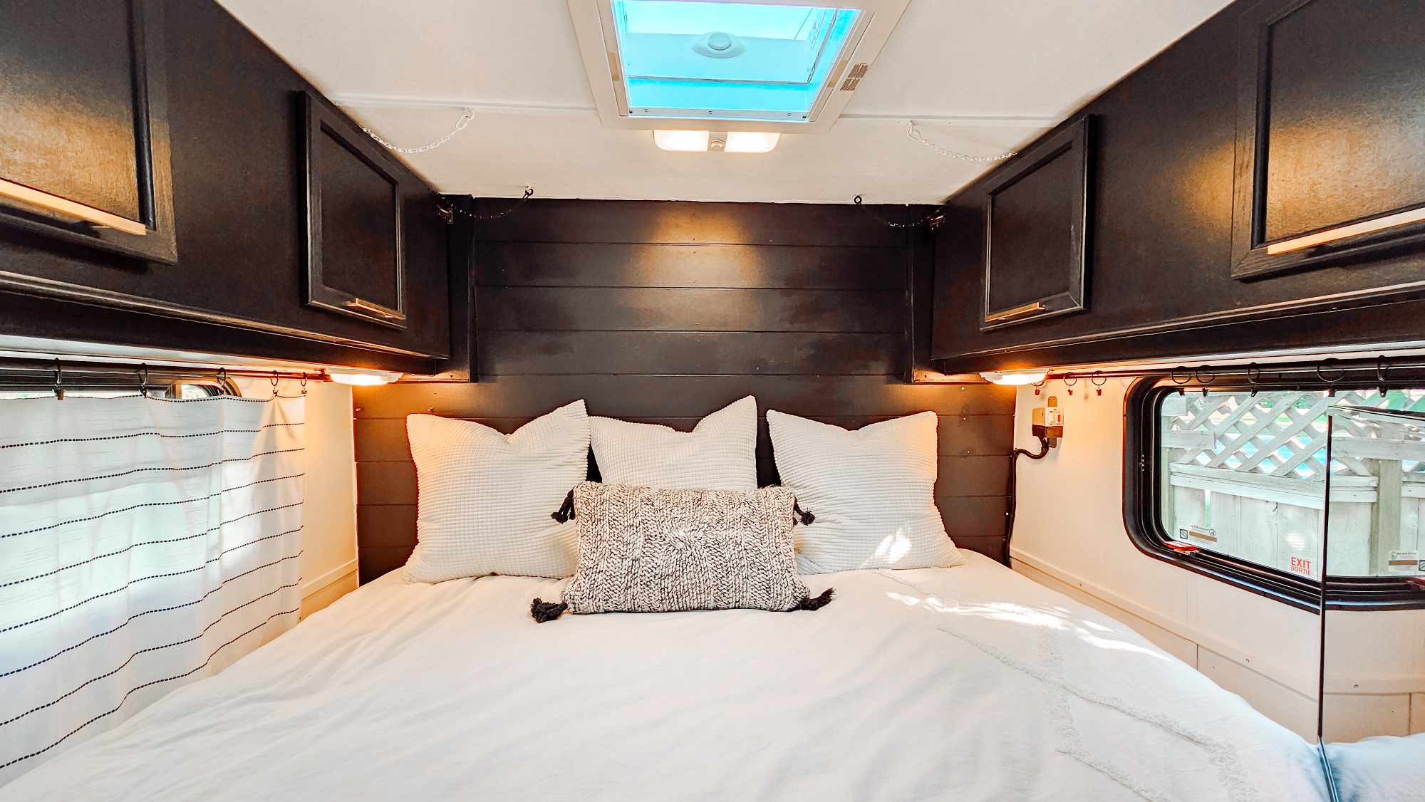 Cozy RV rental bedroom interior. Features a large white bed, dark wood headboard, overhead cabinets, and skylight.. Terry Fleetwood 1991