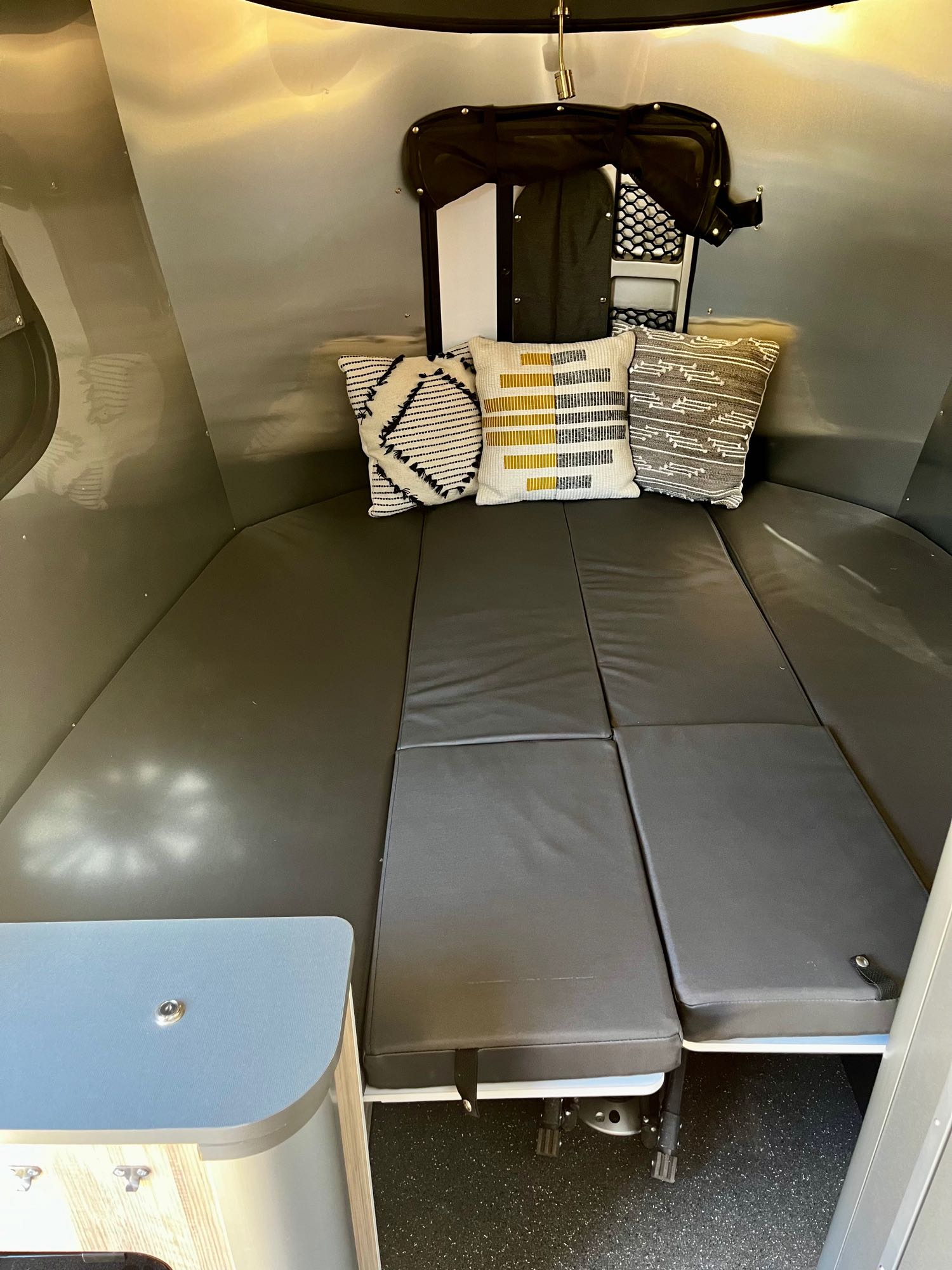 Compact RV rental interior featuring a convertible bed with gray cushions & decorative pillows. Perfect for travel!. Airstream Base Camp 2021