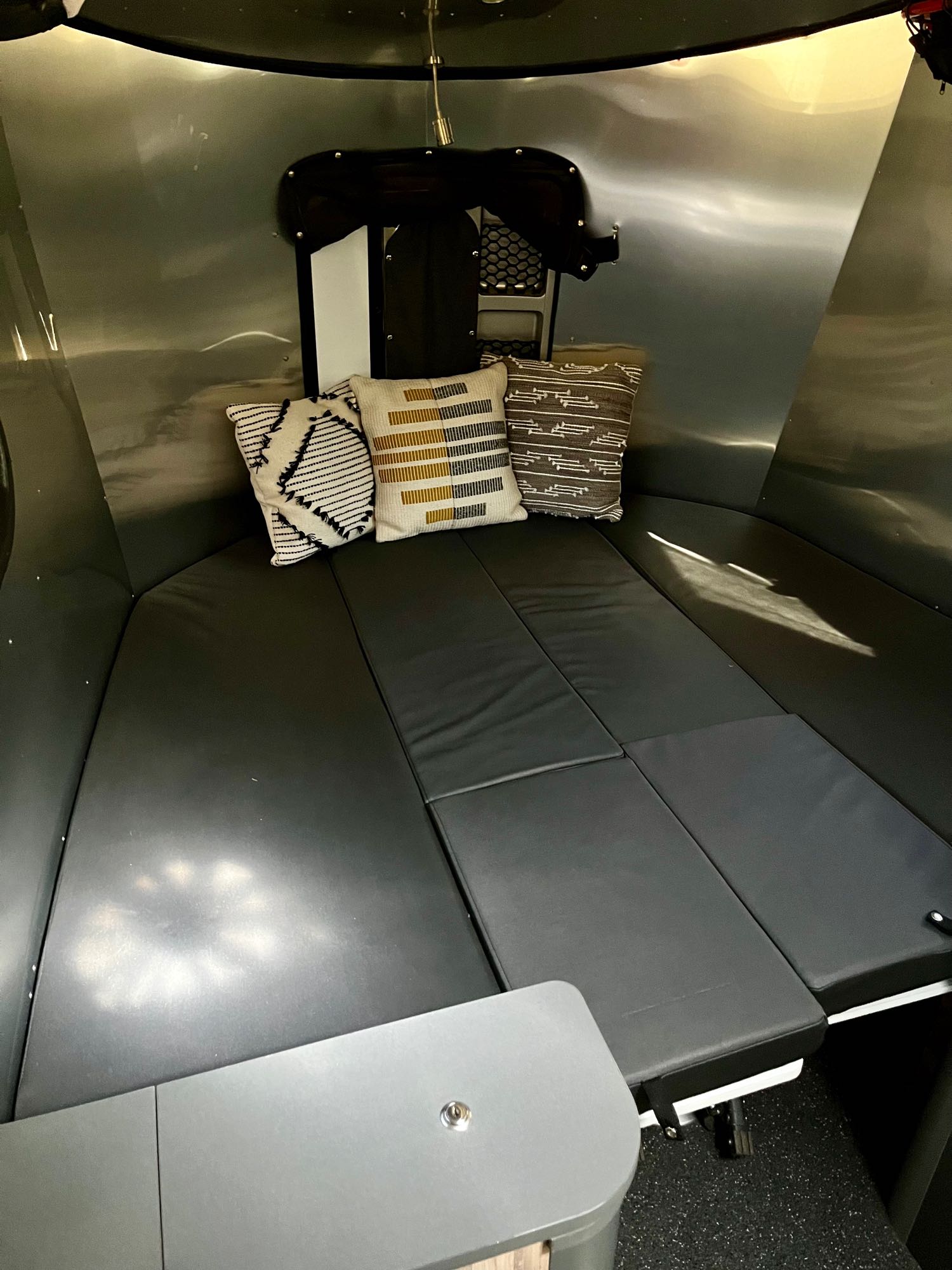 Step into a cozy RV rental: a modern interior with black cushioned seating, throw pillows, and sleek metallic walls.. Airstream Base Camp 2021