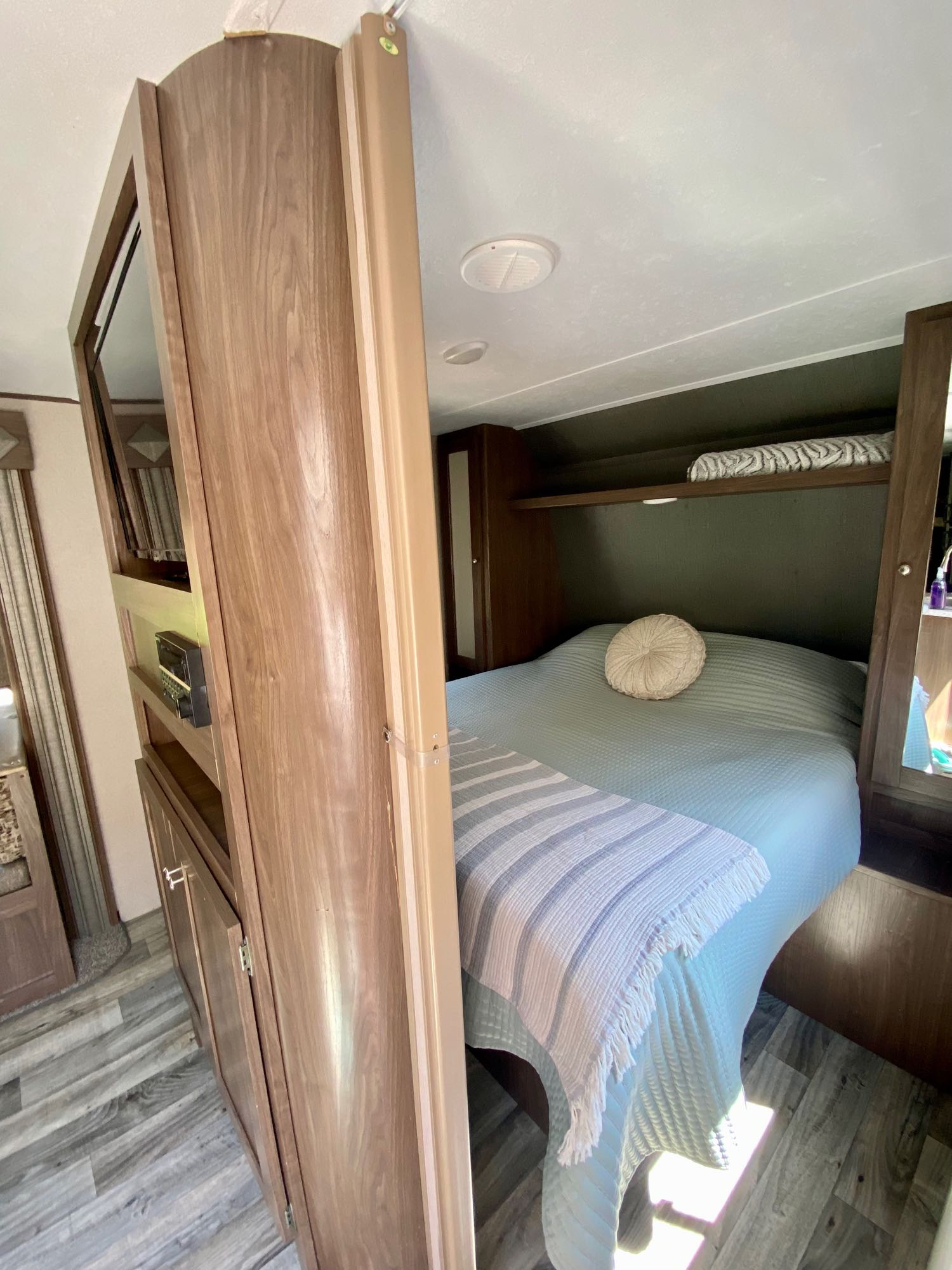 Inside a comfortable RV rental bedroom, featuring a light blue bed, round pillow, and wooden built-in storage.. Keystone RV Hideout 2018