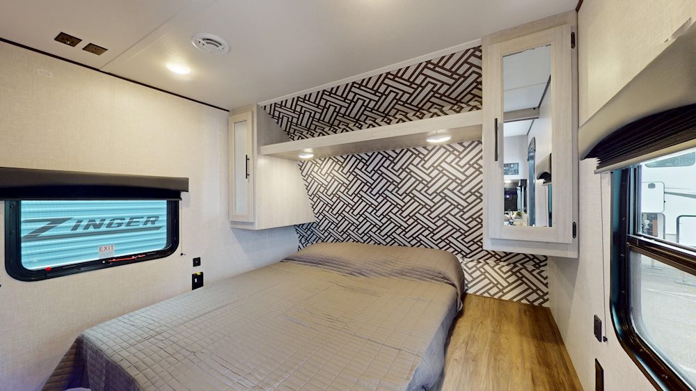 Inside this RV rental, find a bright bedroom with a comfy bed, geometric accent wall, overhead cabinets, and window.. Crossroads RV ZR270BH 2024