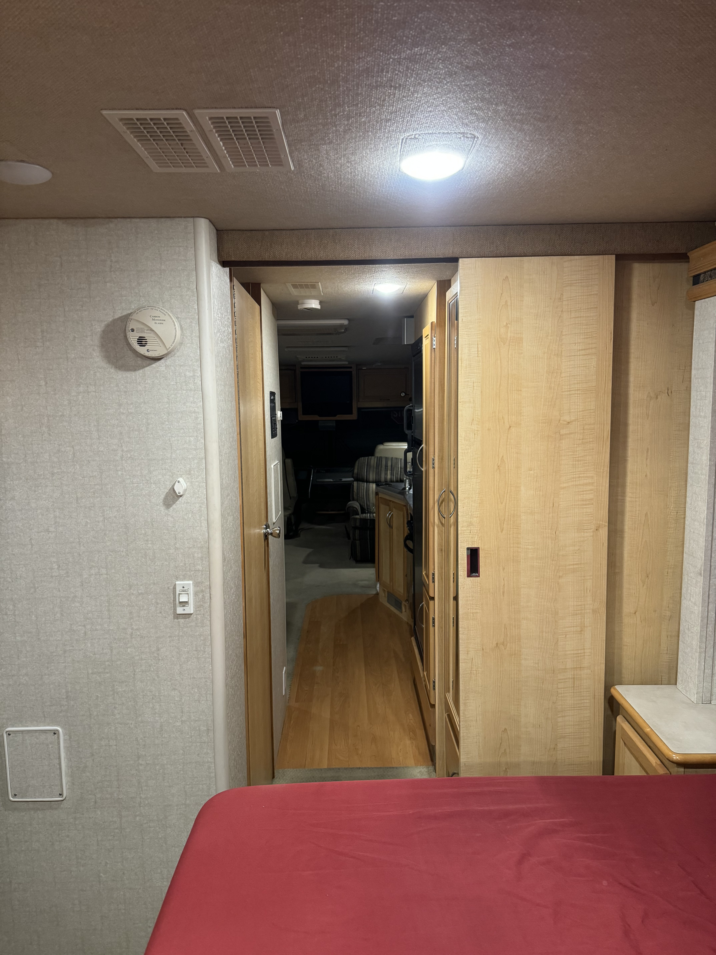 Inside an RV rental: view from the red-covered bed through the aisle, past cabinetry, towards the front cabin.. Fleetwood Sounthwind 2004