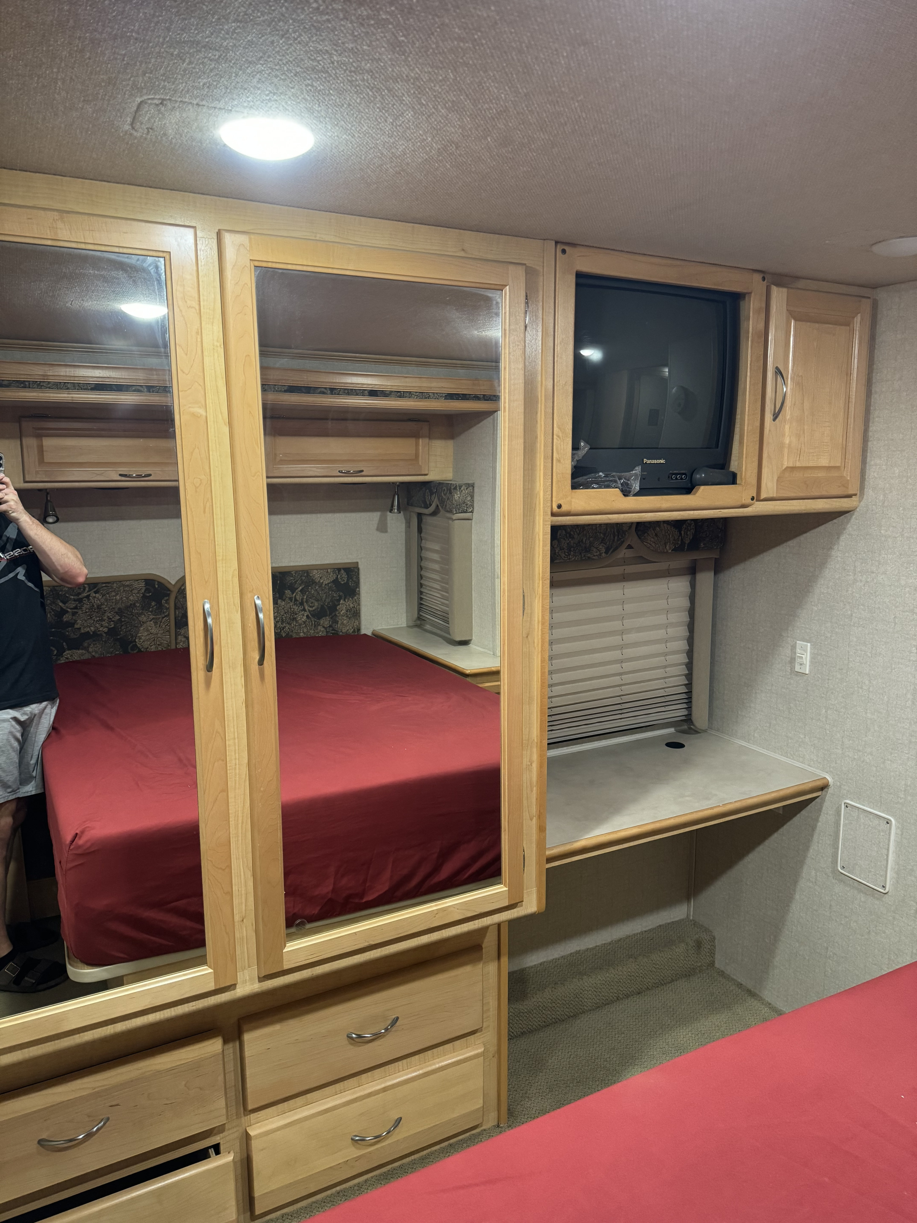 Detailed view of an RV rental bedroom interior, featuring a red bed, mirrored closet, TV, and a compact desk area.. Fleetwood Sounthwind 2004