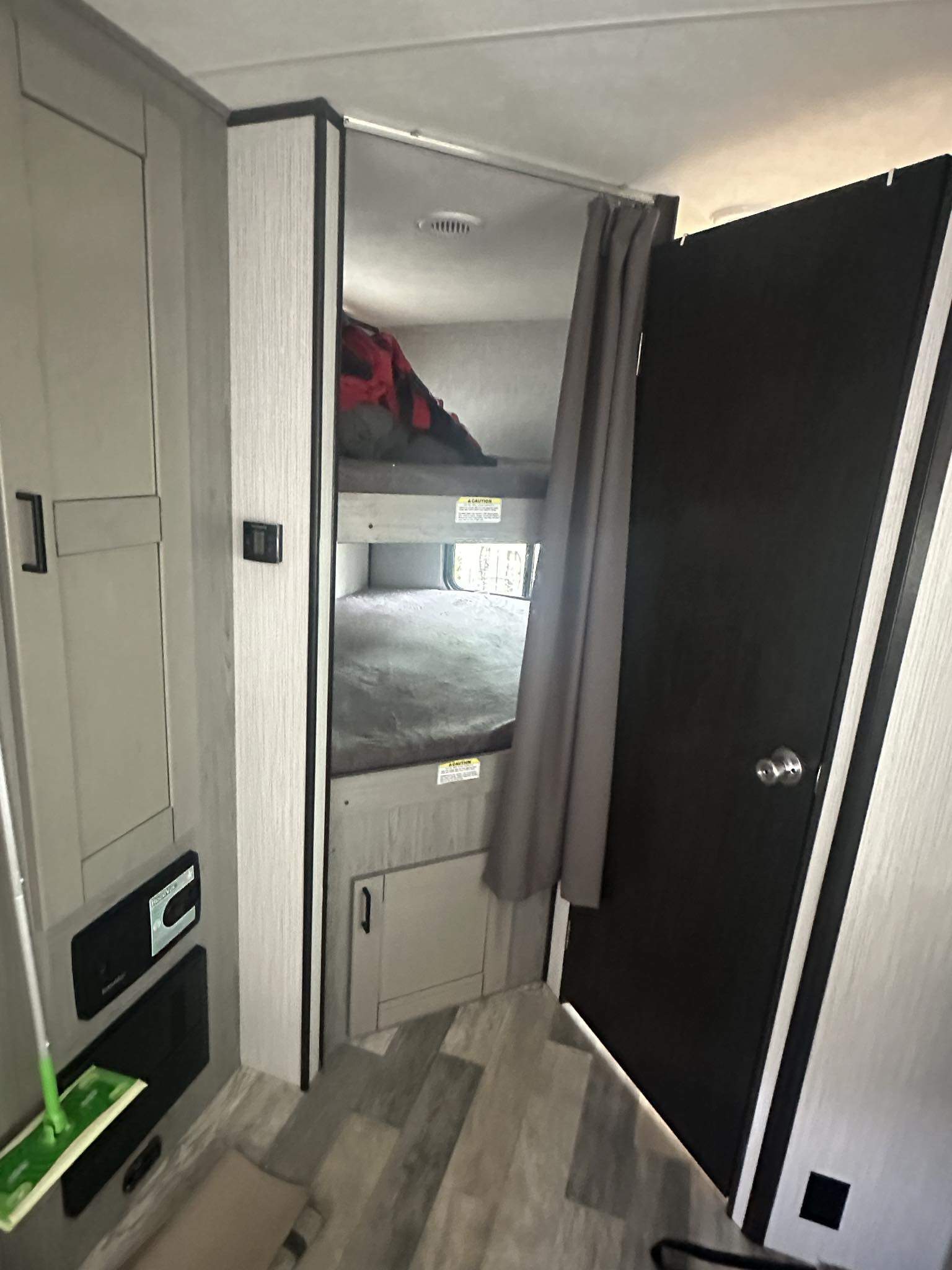 Inside an RV rental, two bunk beds with a privacy curtain and adjacent storage cabinets lead to a dark interior door.. Heartland Mallard 2020