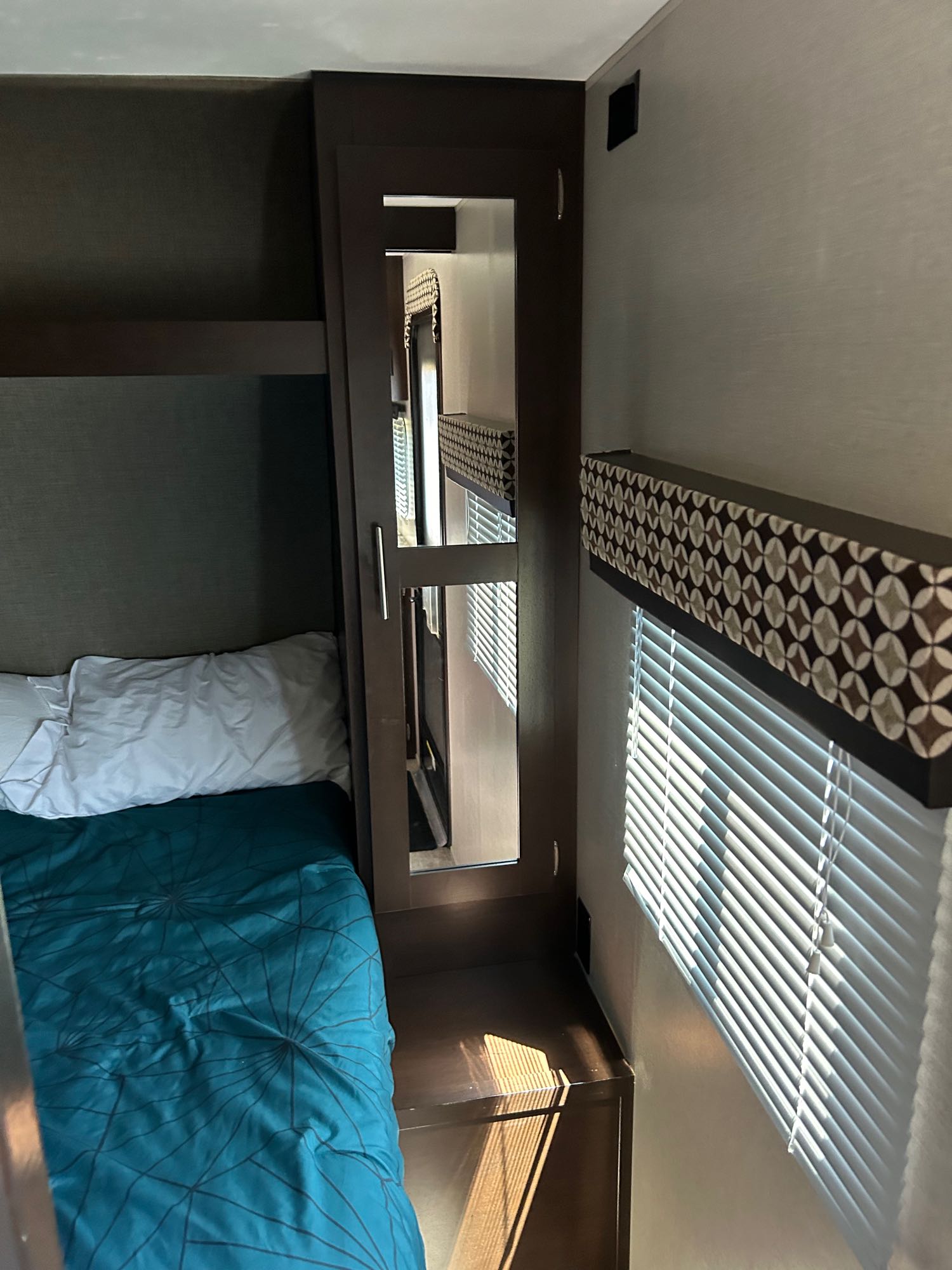 Inside an RV rental: a cozy bunk bed area, mirrored closet, and window with patterned valance and blinds.. KZ 332BHLE 2018