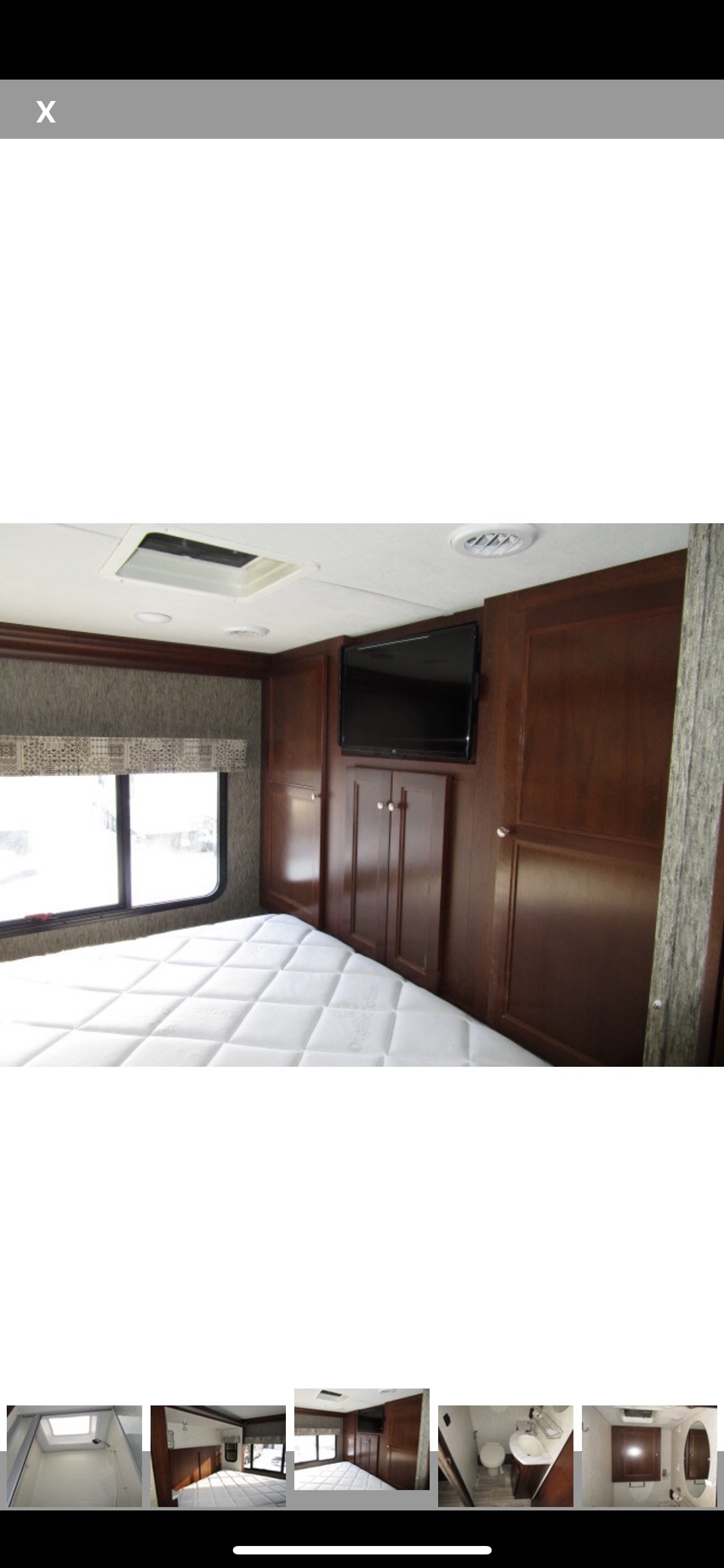 Inside an RV rental: a cozy bedroom awaits with a comfy bed, wall-mounted TV, and dark wood storage.. Forest River Sunseeker 2018