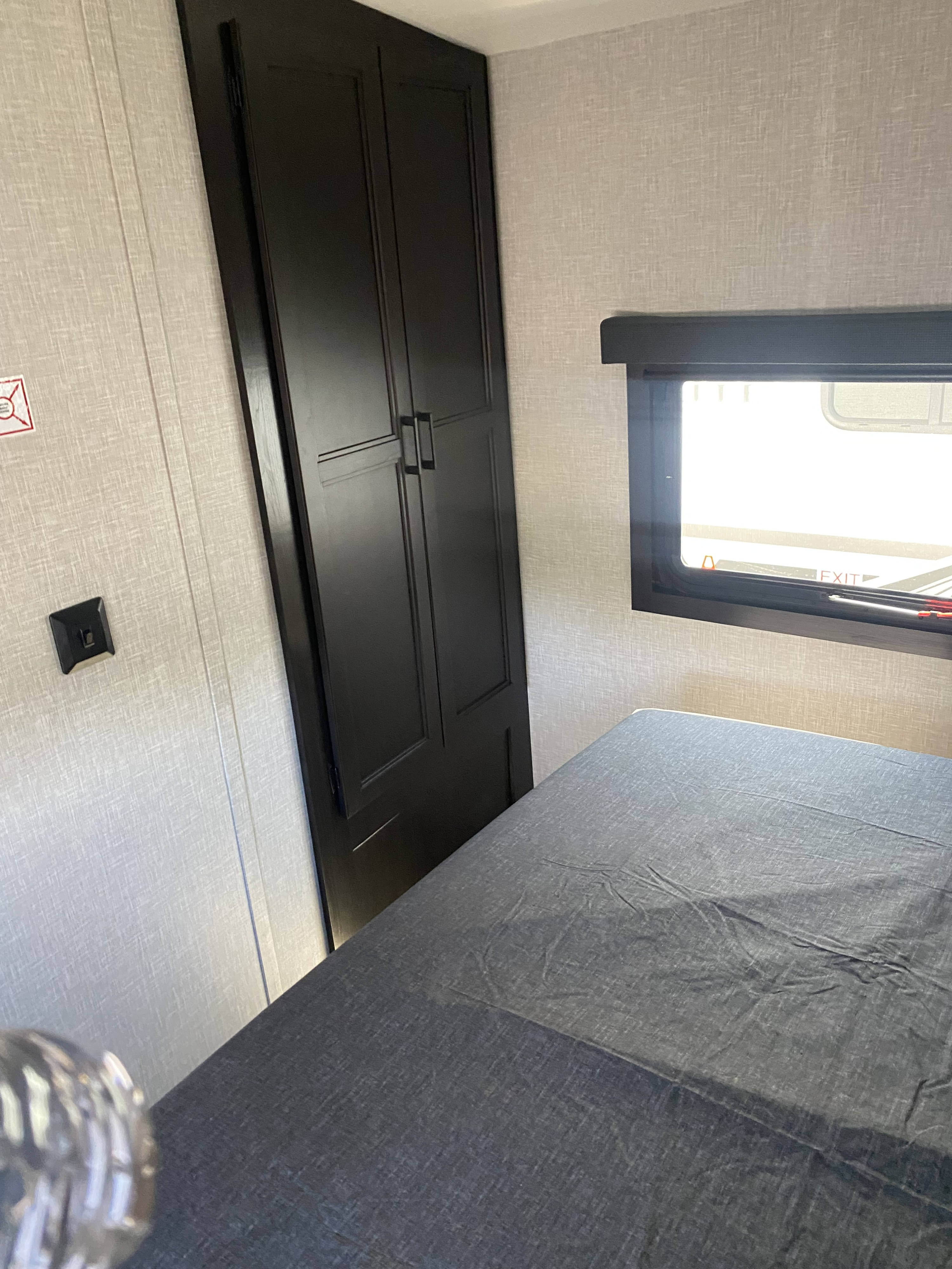 RV rental bedroom showing a dark wardrobe, grey bed, and window. This compact and functional space is ideal for travel.. Highland Ridge RV Open Range Lite 2023