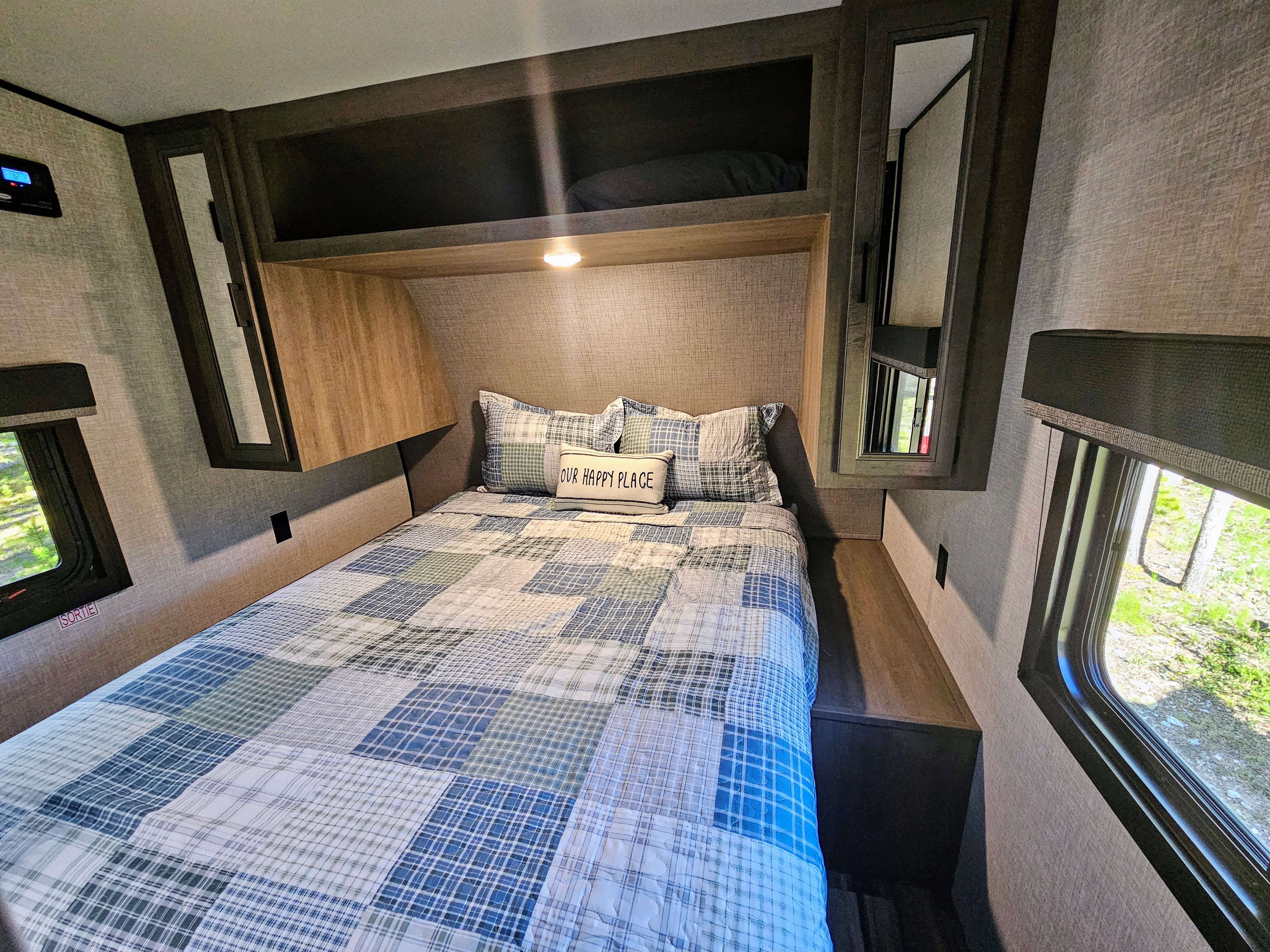 RV rental bedroom: a cozy space with plaid bedding, "Our Happy Place" pillow, overhead storage, and windows for scenic views.. Open Range Open Range 2023