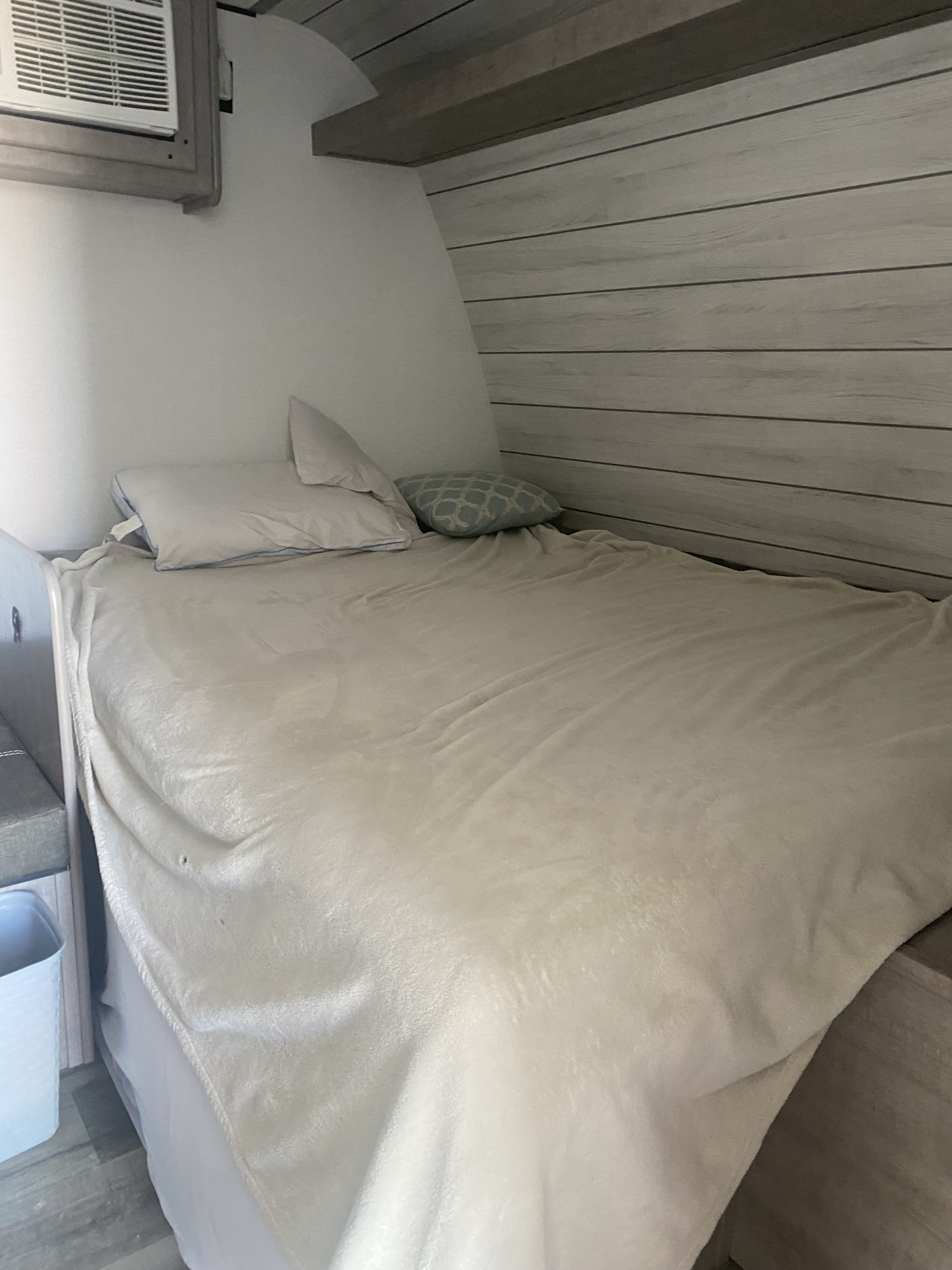 Inside an RV rental: a compact sleeping area with a bed, light blanket, pillows, and wall-mounted AC unit, offering cozy comfort.. Coleman Lantern LT 17b 2024