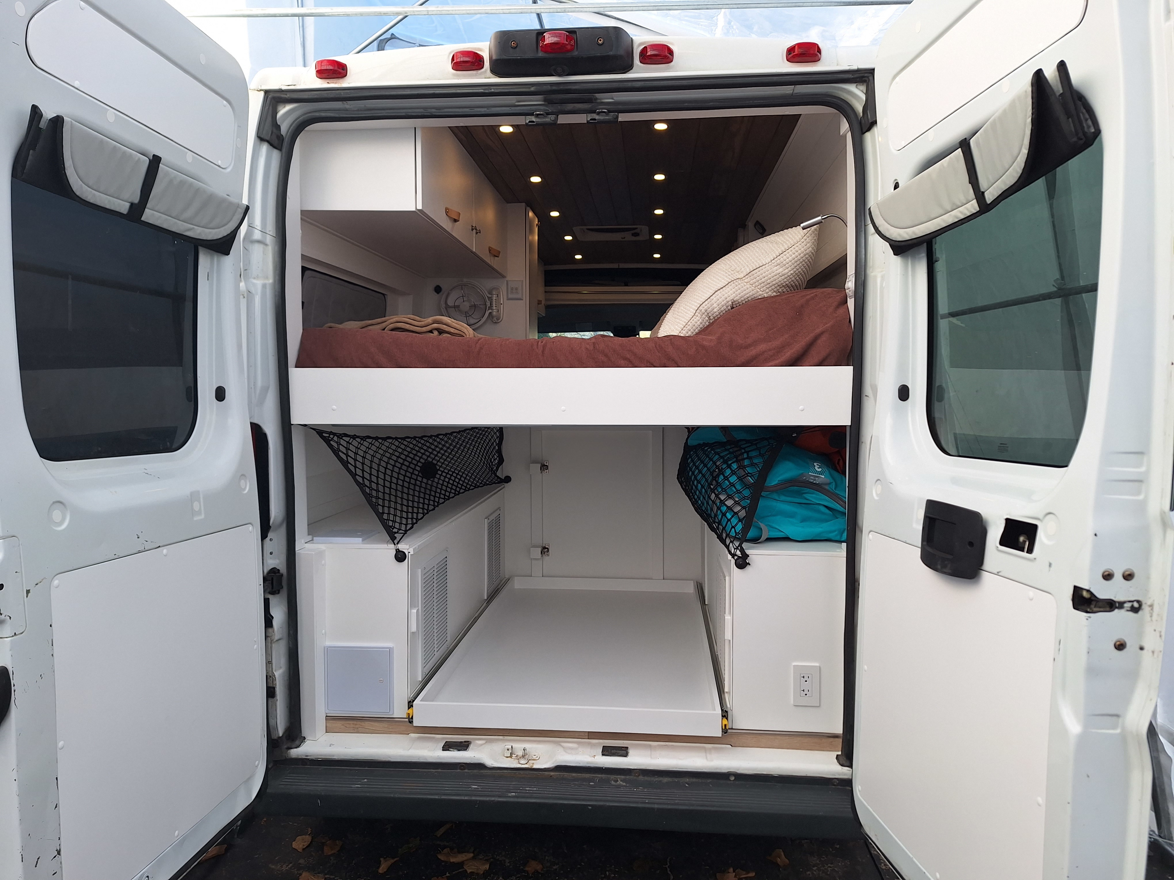 This RV rental shows a custom camper van interior from the rear, with a raised bed, pull-out storage, and organized space.. Ram Promaster Other 2014