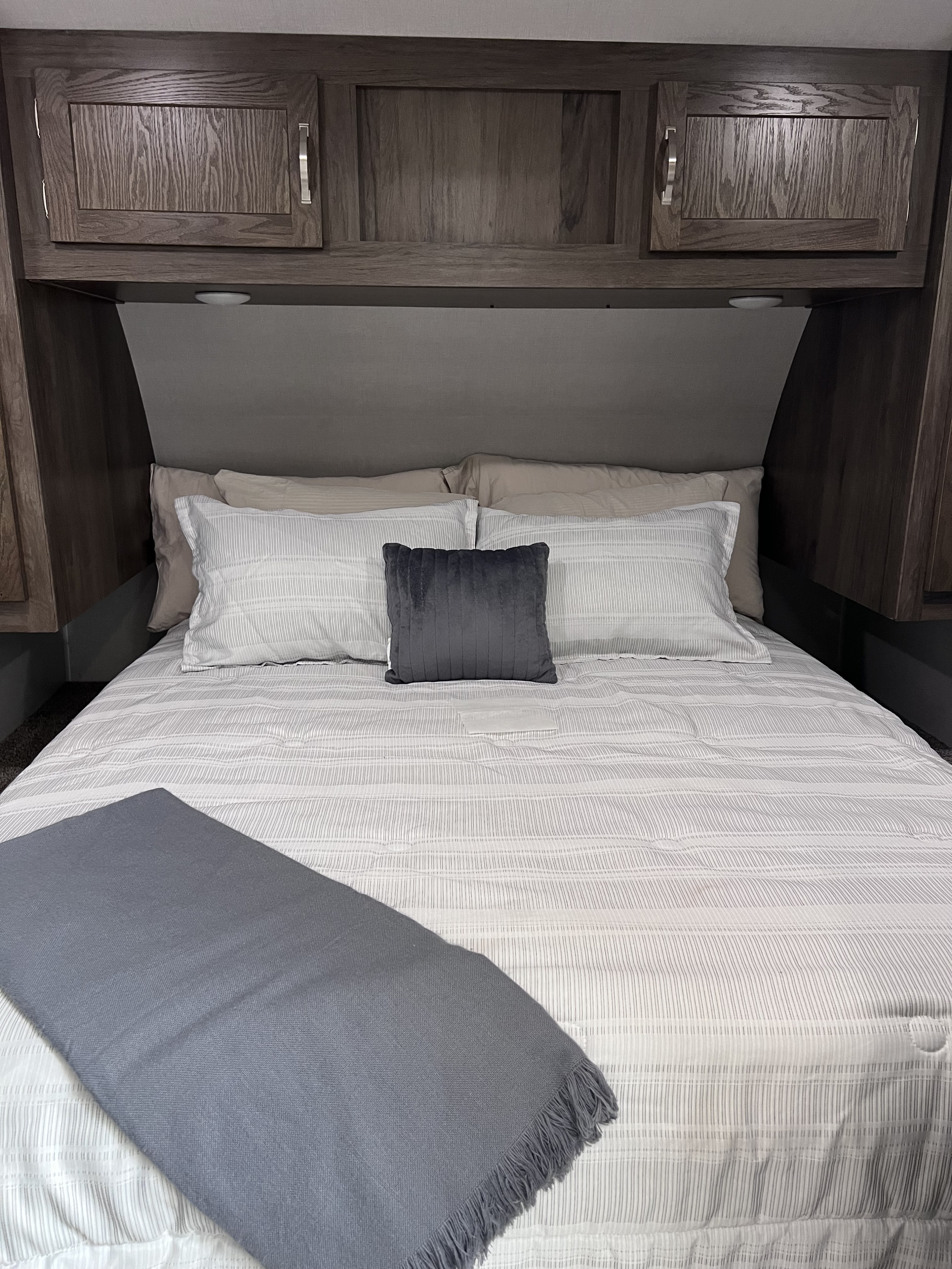Cozy RV rental bedroom showcasing a comfortable bed with striped bedding, a grey throw, and wood cabinets.. East to West Della Terra 2020