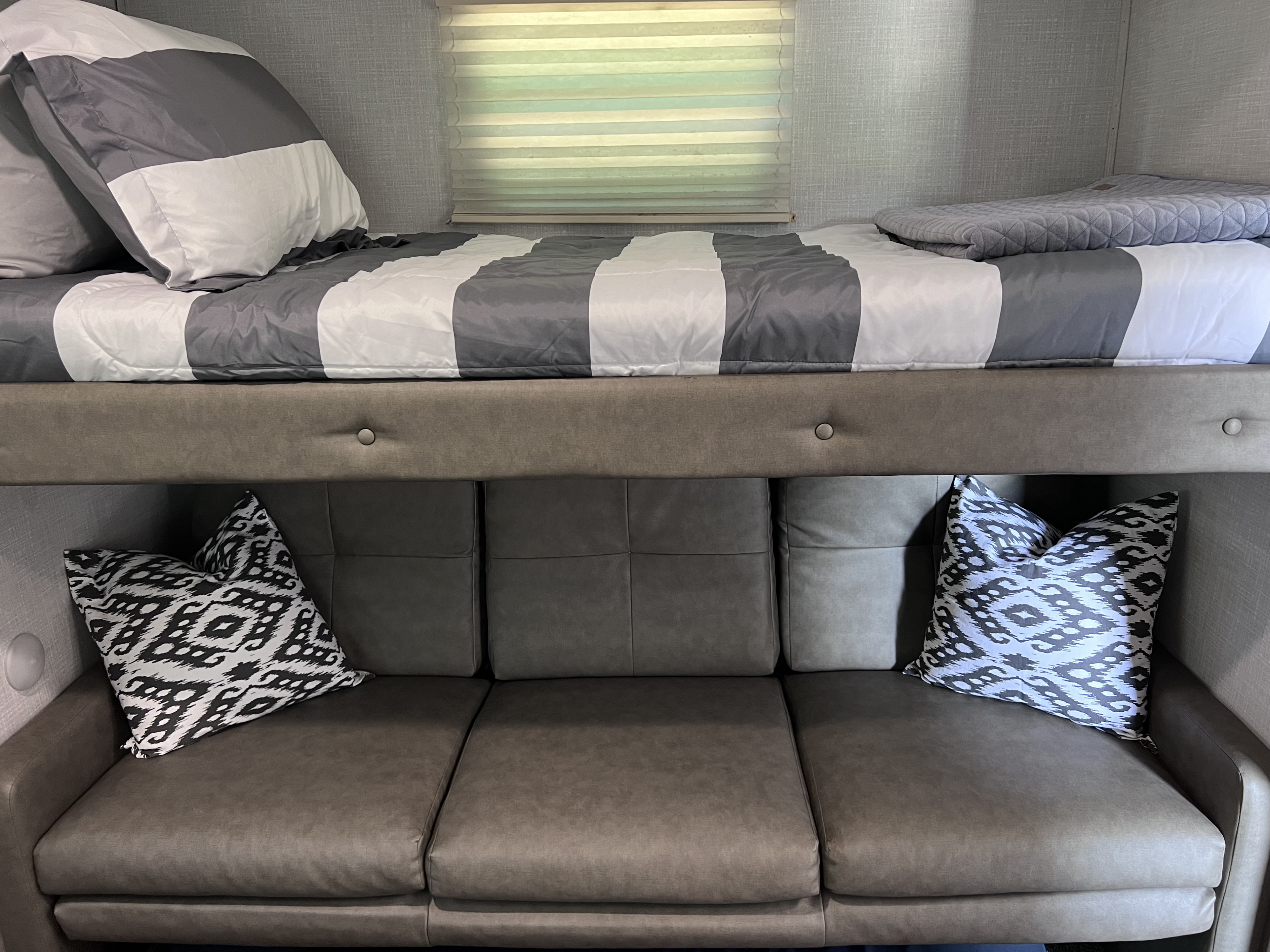 Cozy RV rental interior featuring a gray and white striped bunk bed above a comfortable sofa with decorative pillows.. East to West Della Terra 2020