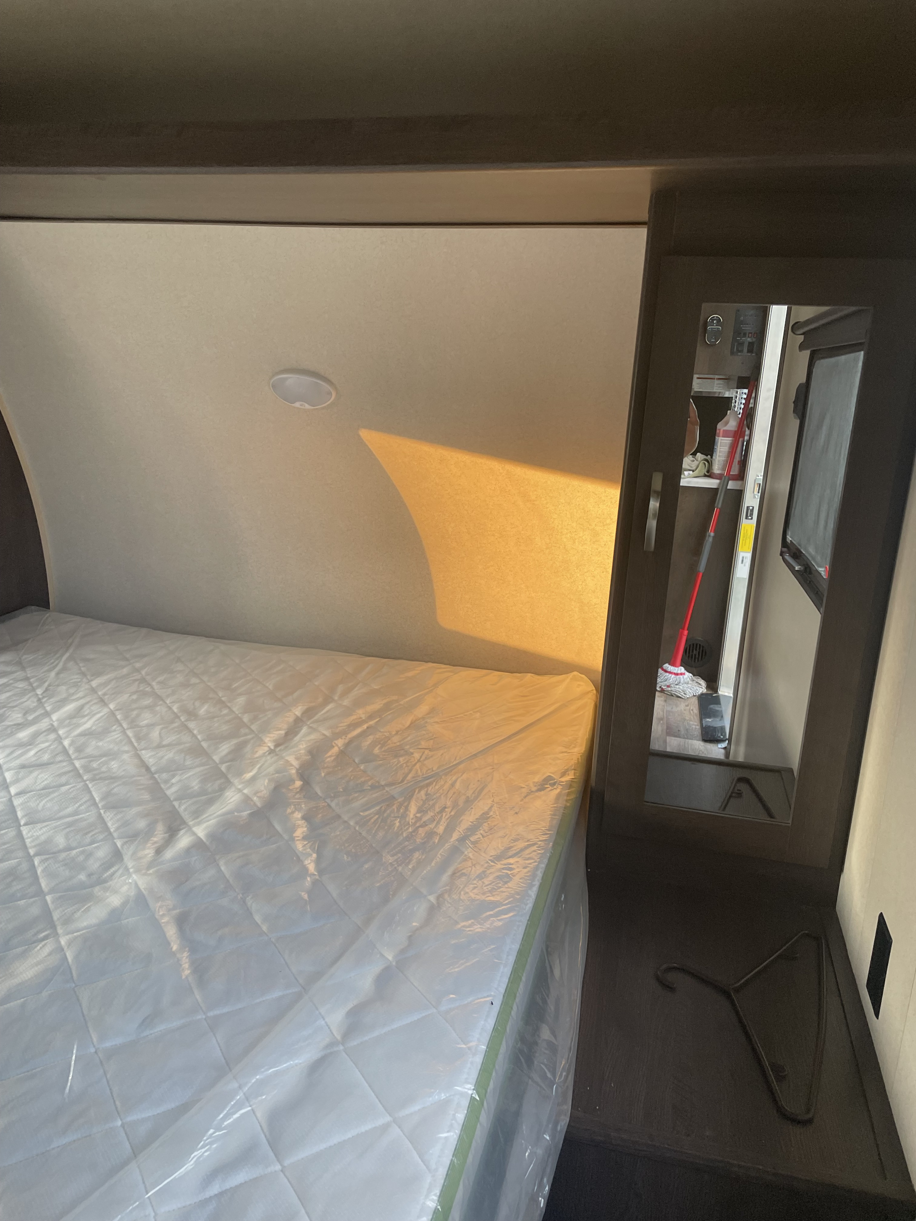 Warm RV rental bedroom with new plastic-wrapped mattress, sunlight, and mirrored closet reflecting a mop.. Forest River Salem Cruise Lite 2019