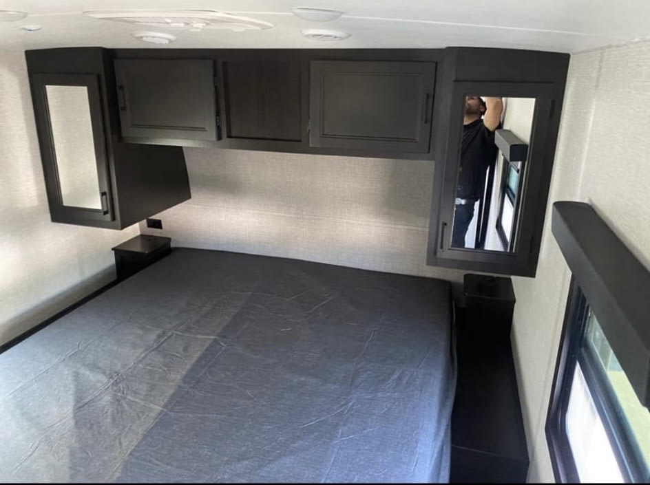 RV rental bedroom interior: dark cabinets, a bed with grey cover, and mirrored closets.. Highland Ridge RV Open Range Lite 2023