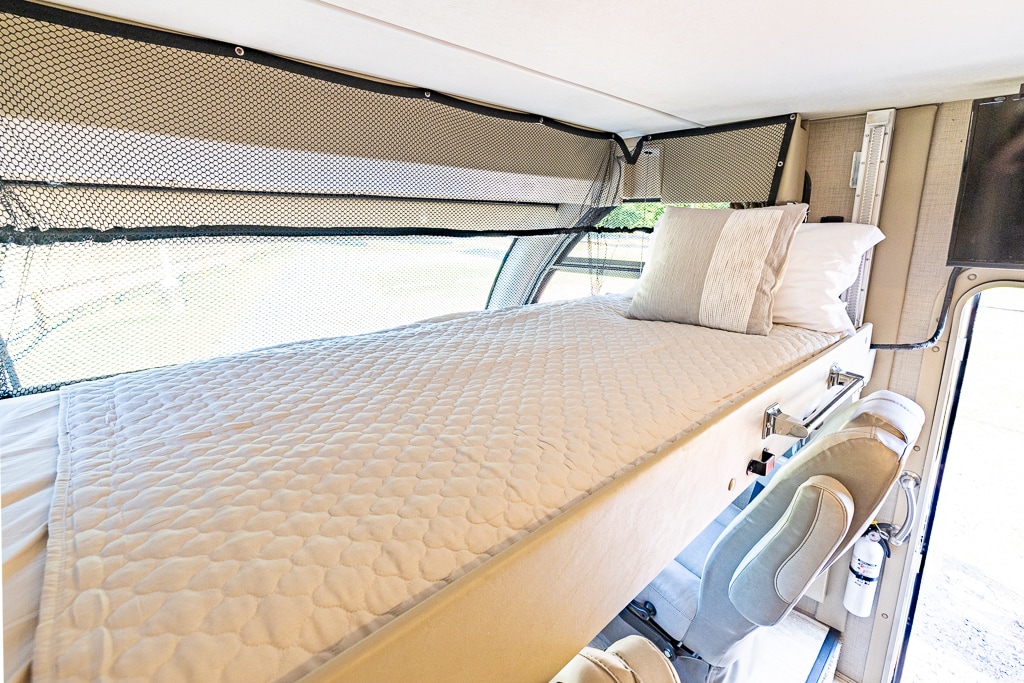 Explore comfort! This RV rental offers a bright, cozy sleeping area with a quilted bed, pillows, and safety netting by the window.. Thor Vegas 2018