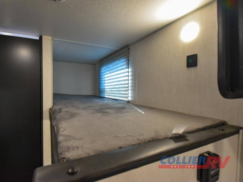 An RV rental bunk bed, featuring a grey mattress, window with blinds, and wall-mounted light for comfortable sleeping.. Forest River Cherokee Wolf Pup 2022