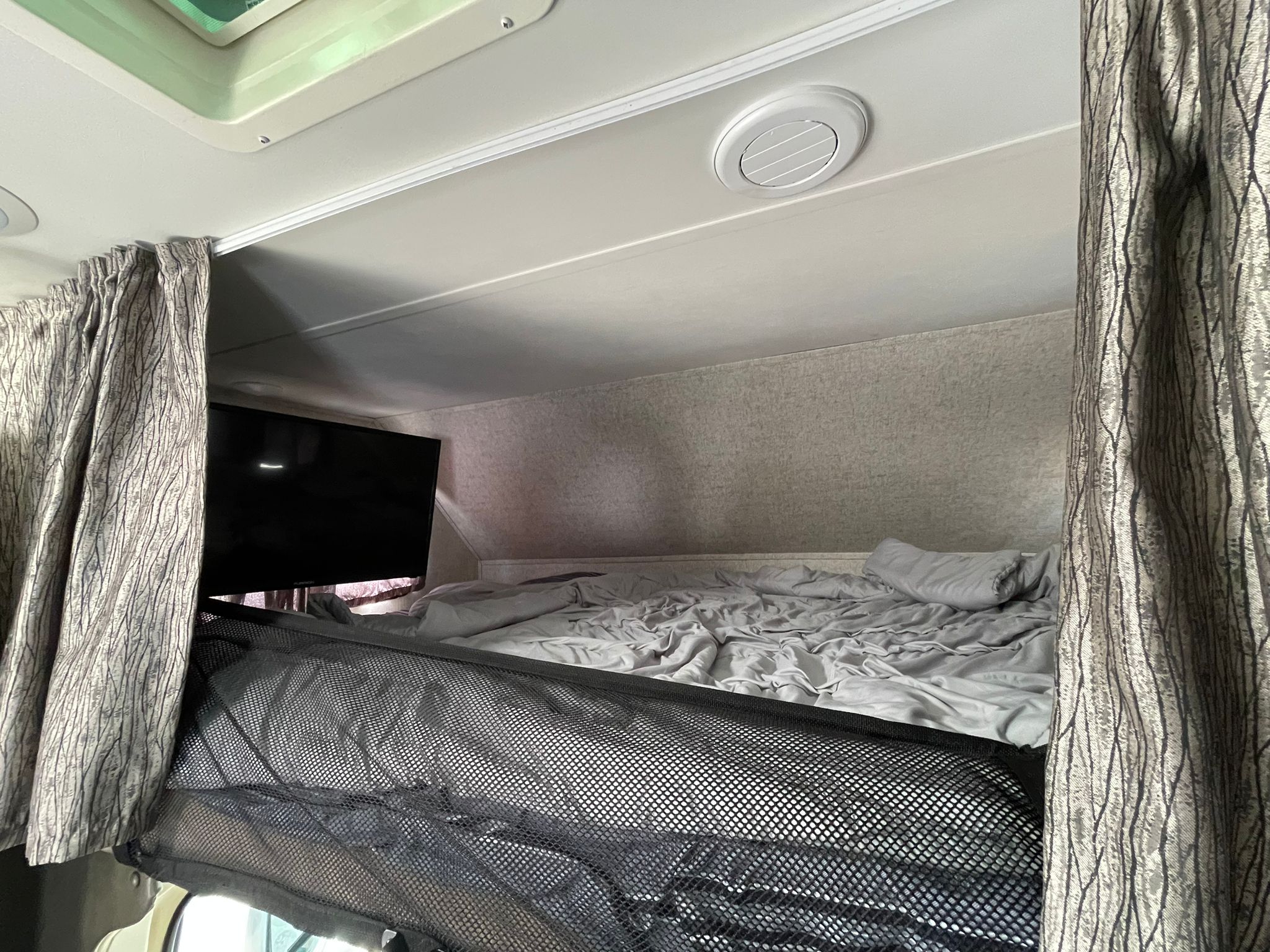 Inside an RV rental, a compact sleeping area features a bed, TV, mesh safety barrier, and privacy curtains.. Forester Forester Motorhome 2017