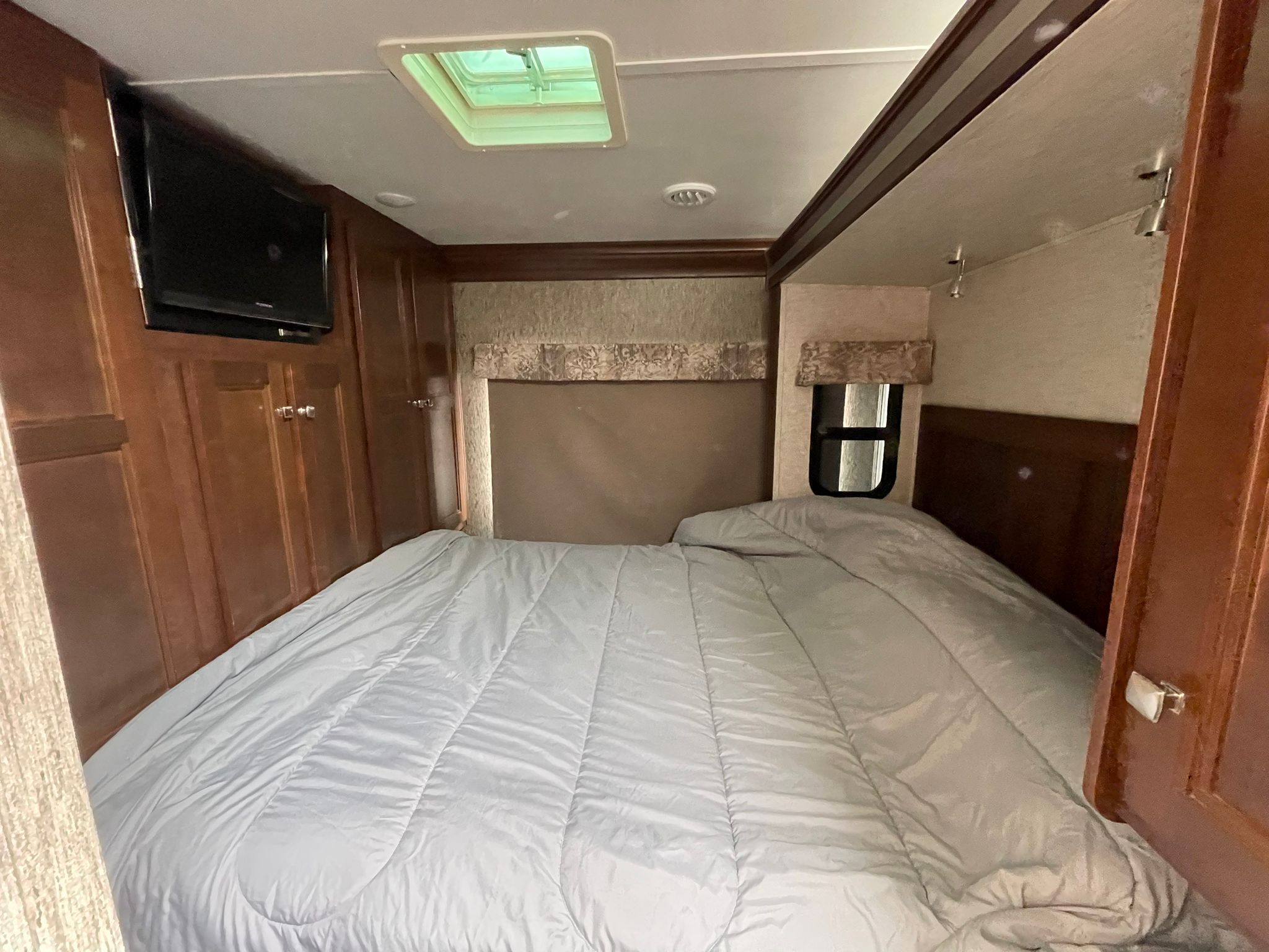 Cozy RV rental bedroom featuring a comfortable bed, wall-mounted TV, ceiling skylight, and storage cabinets.. Forester Forester Motorhome 2017