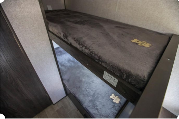 RV rental features two plush, grey bunk beds, each with a dog bone accent, ideal for pets or compact sleeping space.. Dutchmen Coleman Lantern 2021
