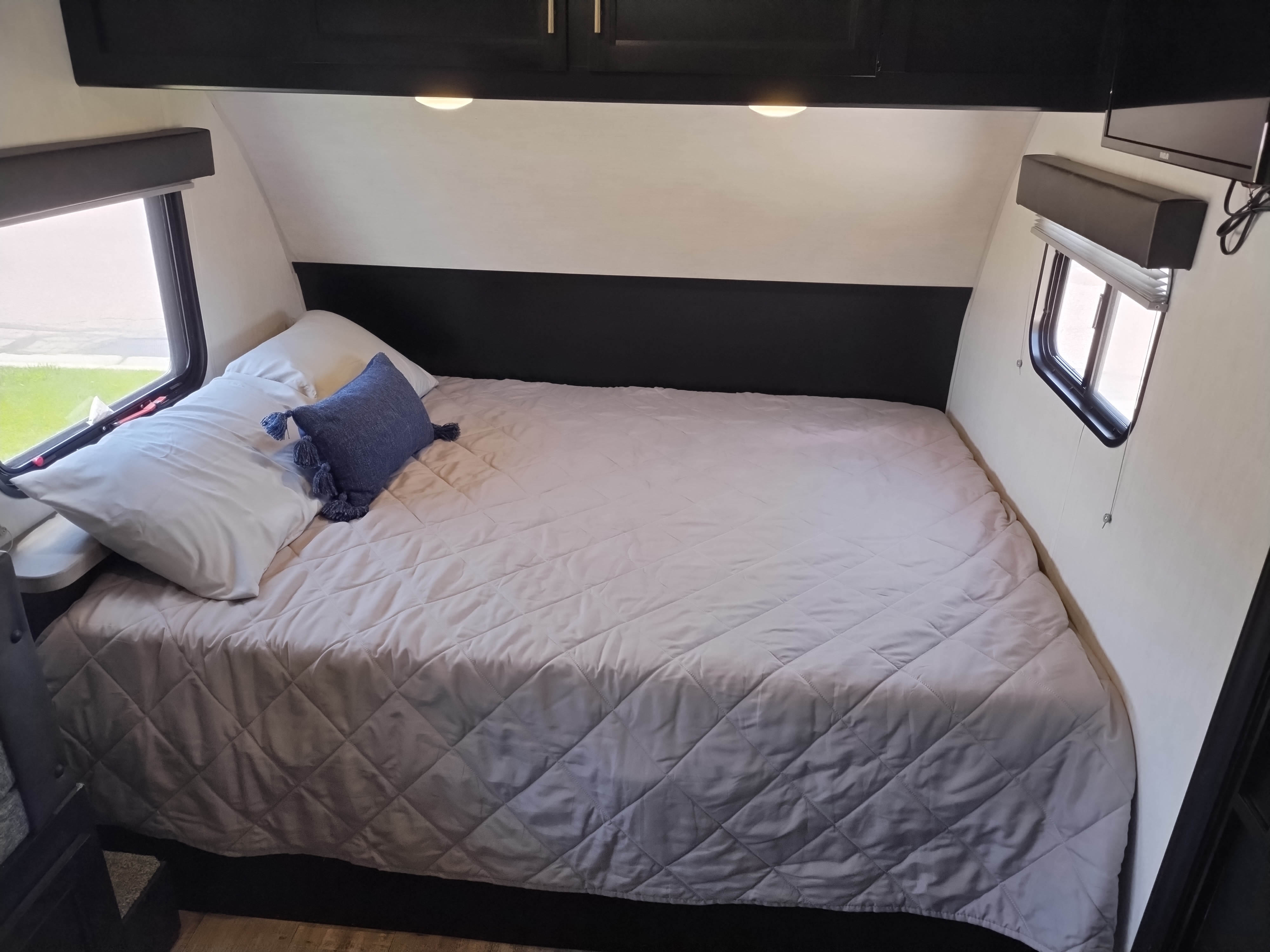 Inside a clean RV rental bedroom featuring a comfy bed with quilted cover, side windows, and overhead lighting.. Forest River Cherokee Wolf Pup 2022