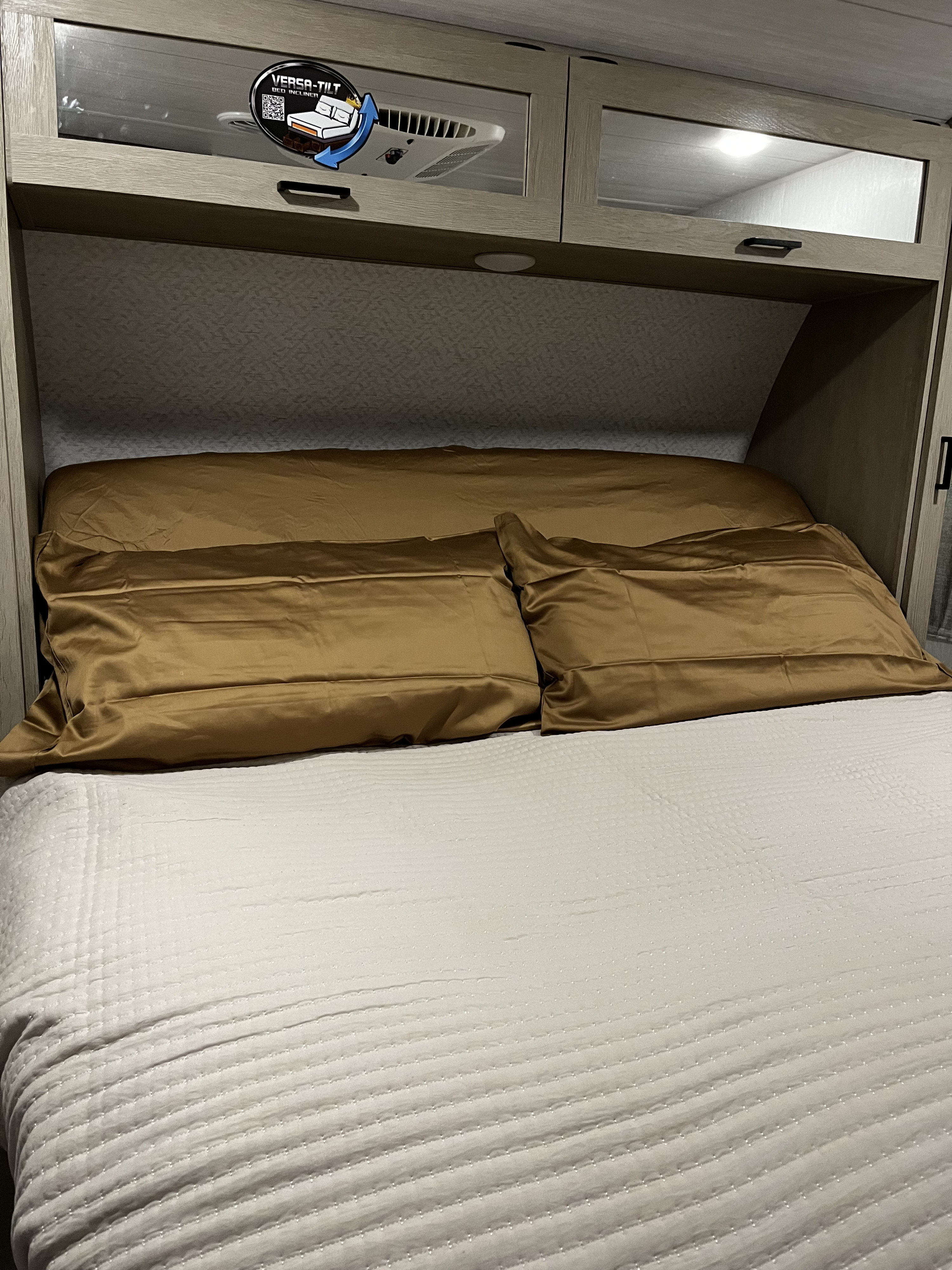 Bright RV rental bedroom showcasing a comfortable bed with golden pillows, sleek overhead cabinets, and an adjustable bed feature.. Forest River Wildwood Platinum 2024