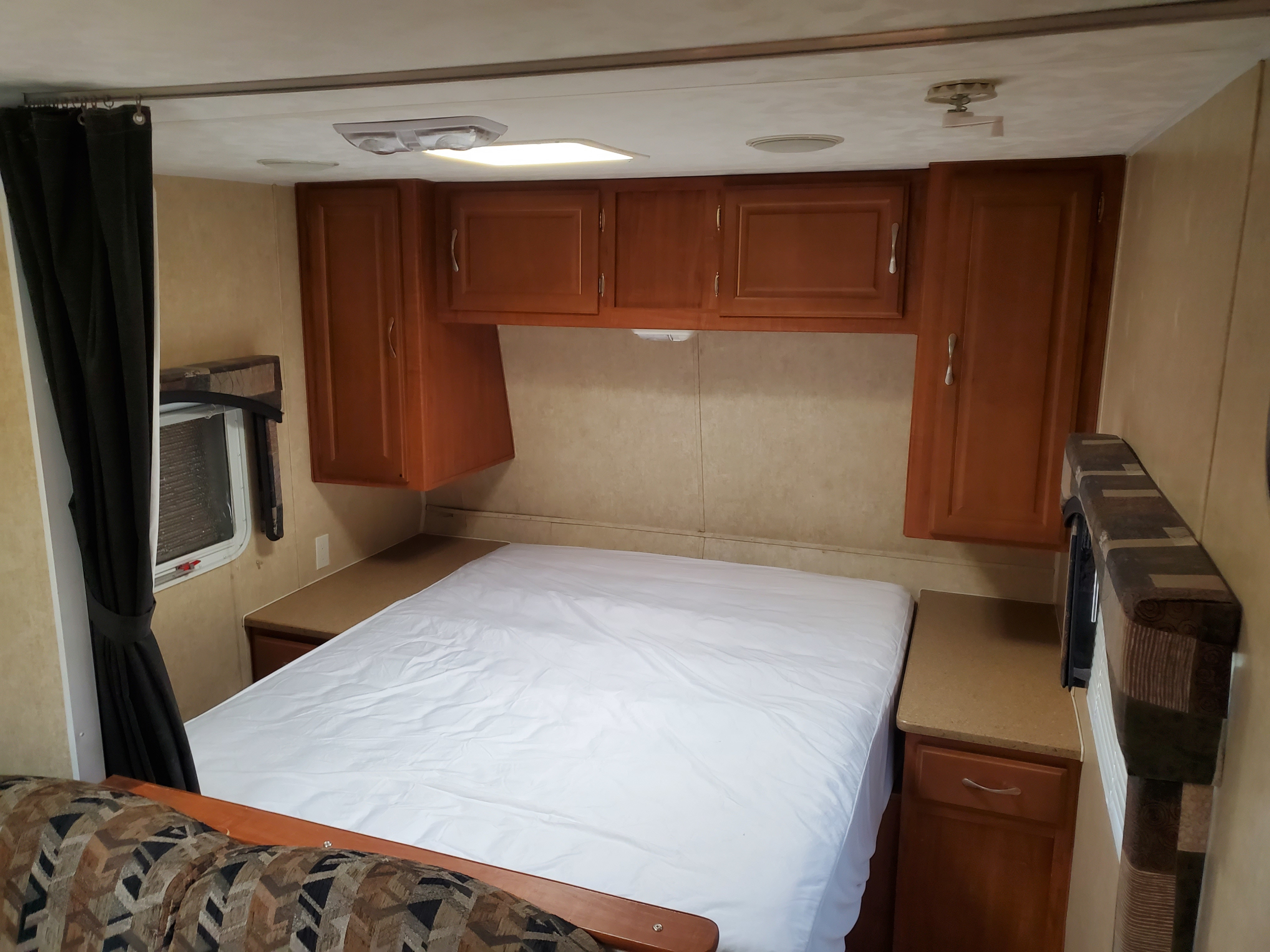 Cozy RV rental bedroom features a white bed, wood cabinets, and window with a dark curtain.. Forest River Salem 2009
