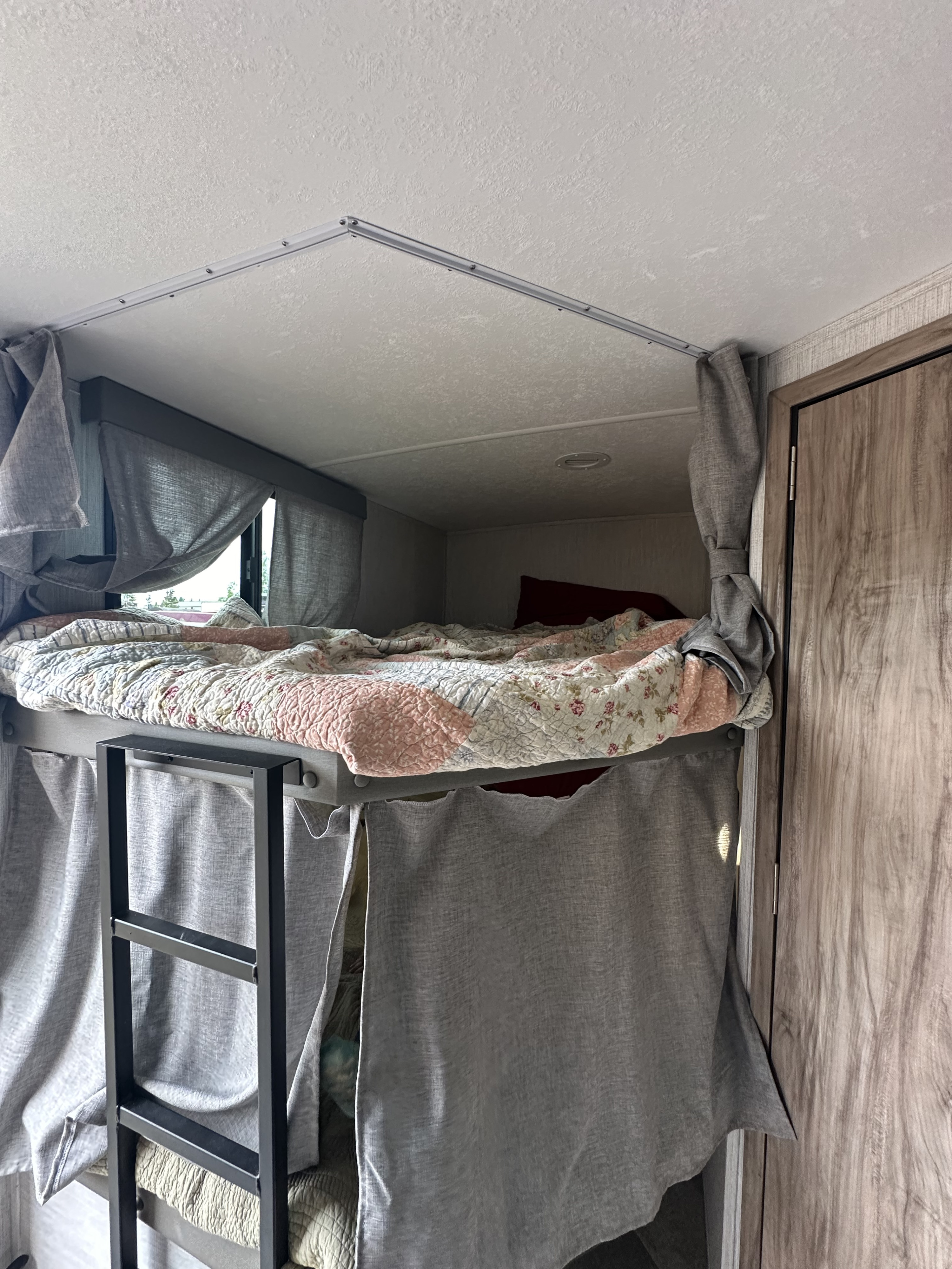 Inside an RV rental: a comfortable bunk bed with a floral quilt, privacy curtains, and a metal ladder.. Palomino Solaire Ultra Lite 243BHS 2022
