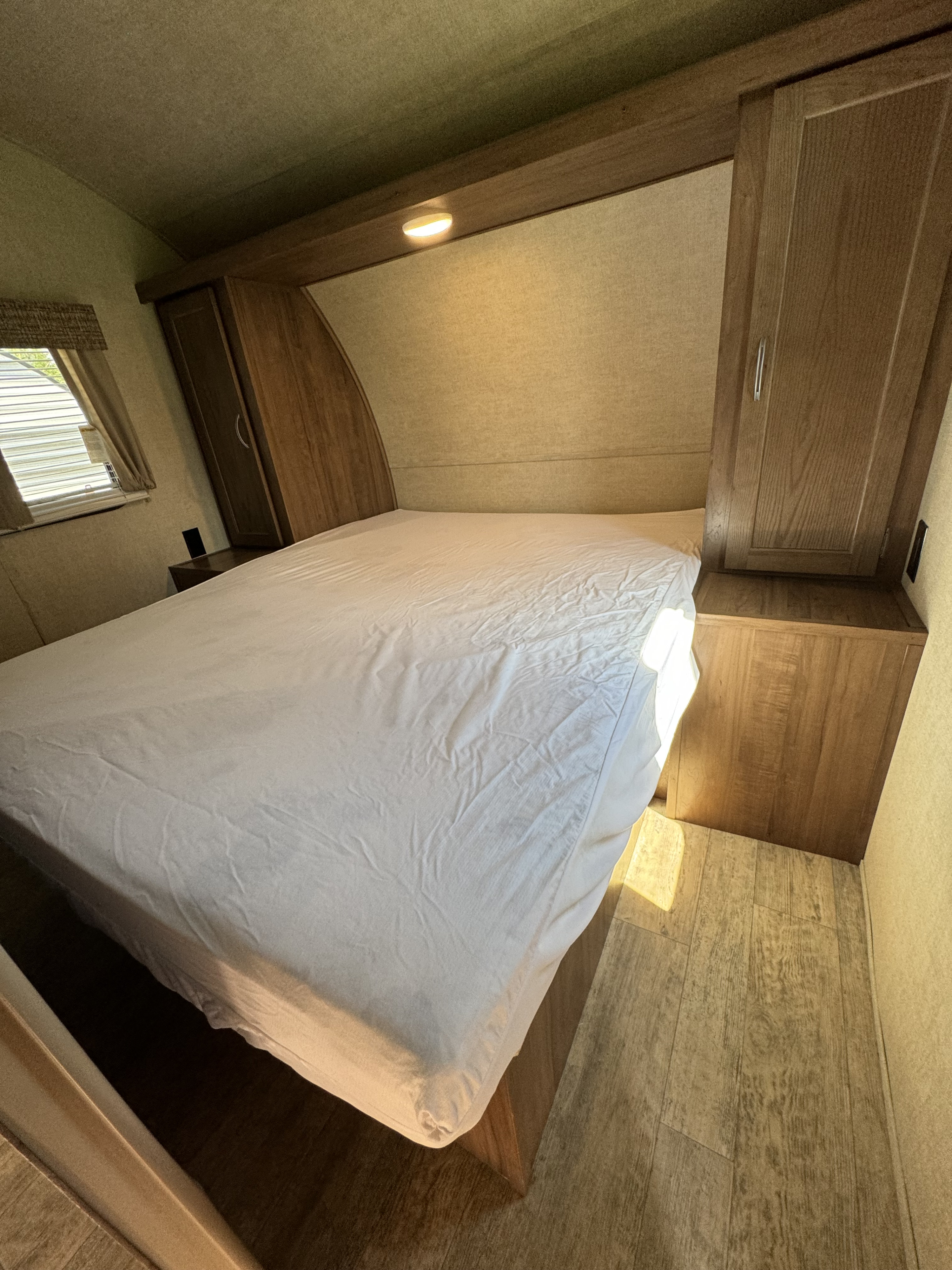 This RV rental bedroom offers a comfortable bed with white sheets, built-in cabinets, and wood-look flooring.. Gulf Stream Ameri-Lite 2018