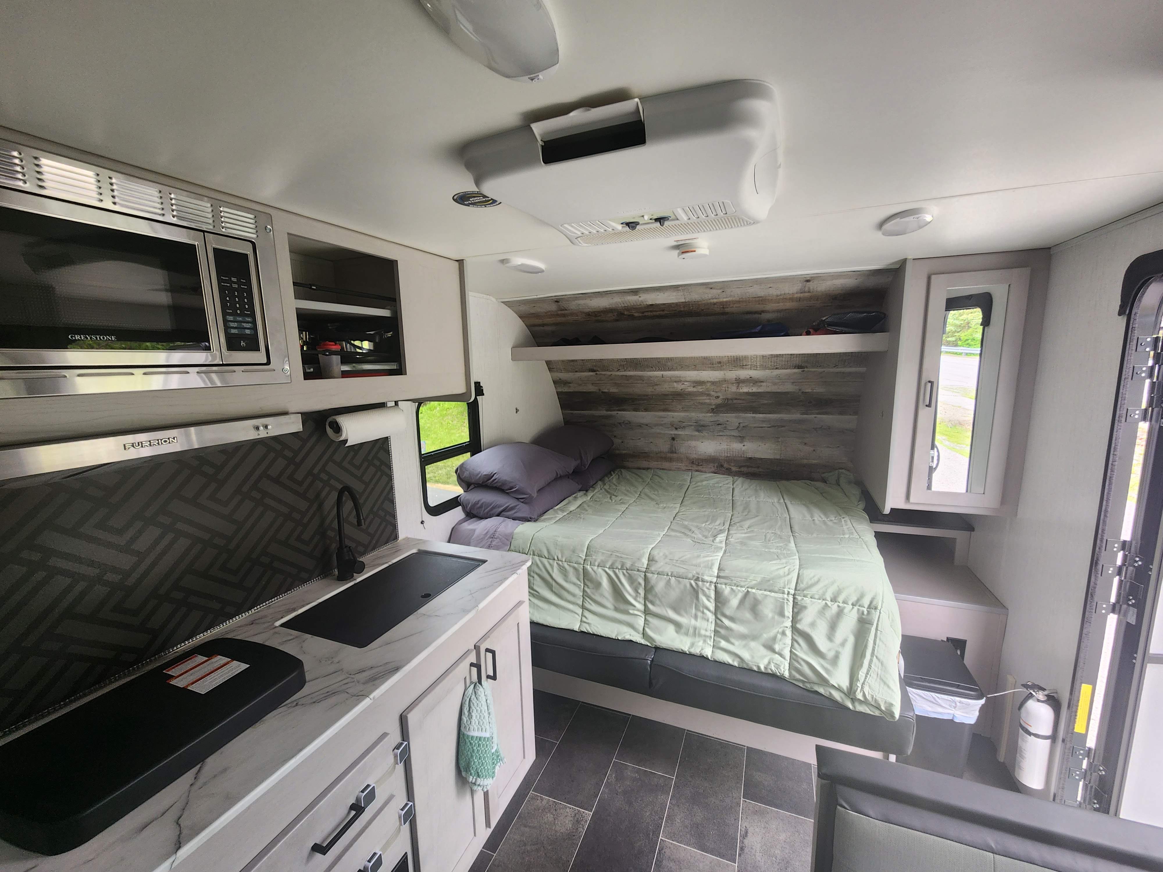 Modern rv rental interior with a compact kitchen featuring a microwave, sink, and a cozy bed with a green comforter.. Heartland RVs Mallard 2022