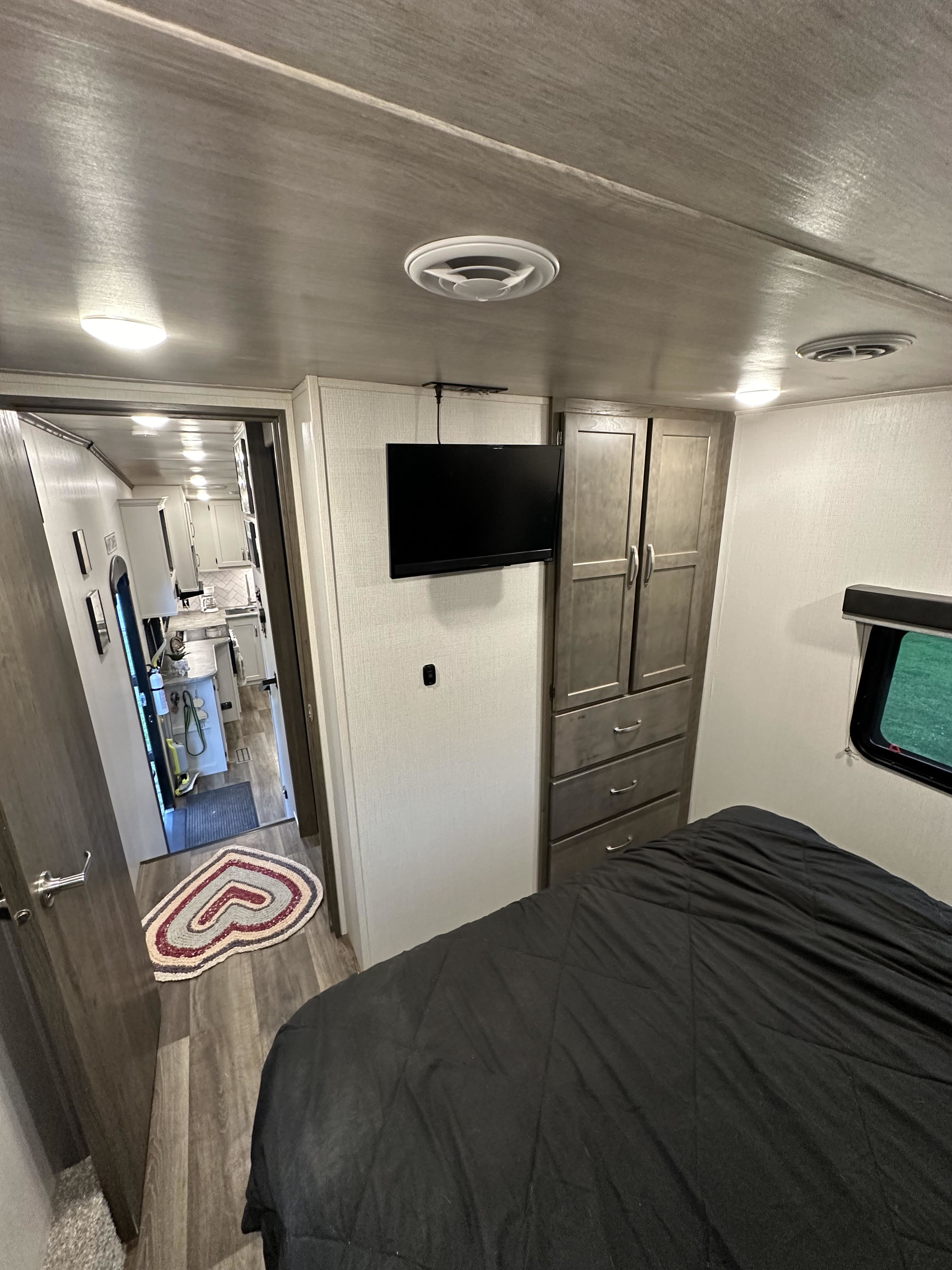 Inside an RV rental: modern bedroom with TV, leading to a functional kitchen/living space, showcasing its comfortable interior.. Keystone RV Cougar 2023