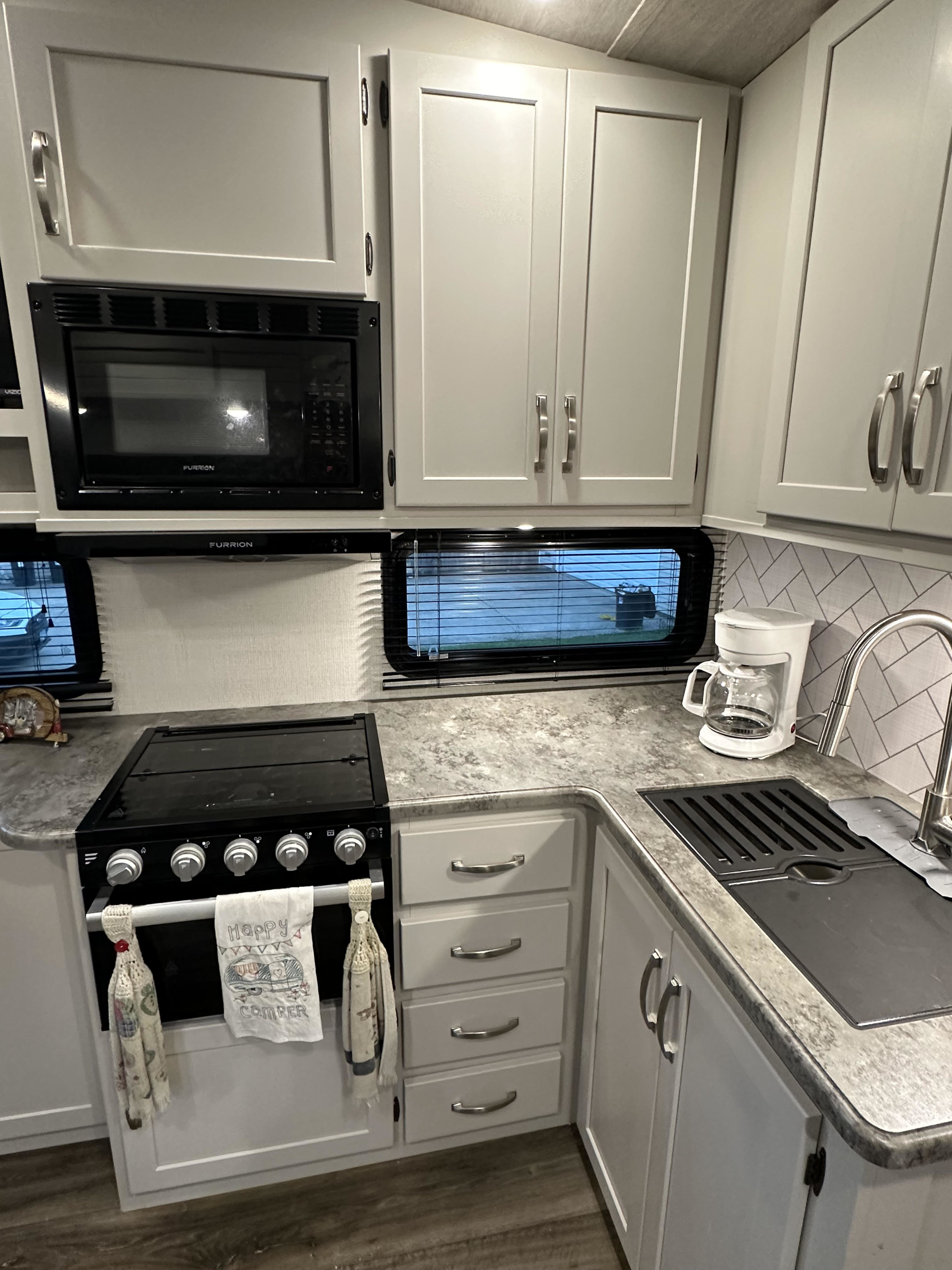 Modern RV rental kitchen featuring light grey cabinets, a microwave, stove, sink, and coffee maker, perfect for road trips.. Keystone RV Cougar 2023