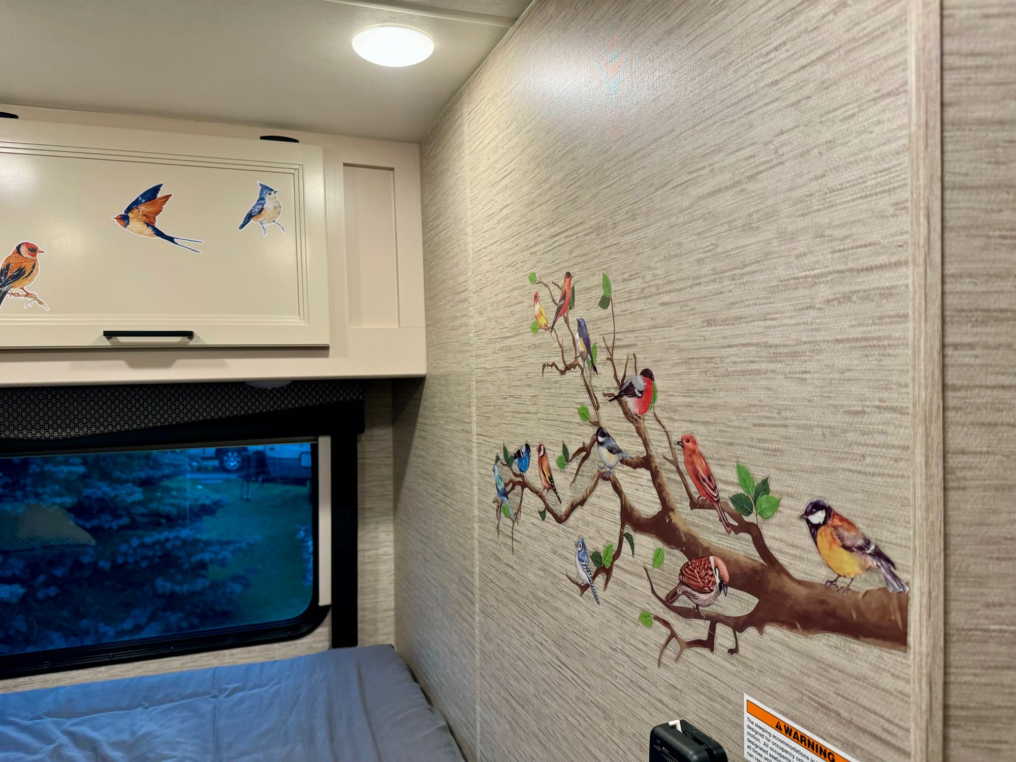 Cozy RV rental interior featuring charming bird decals on the wall, a comfortable bed, and a cabinet. Perfect for nature lovers.. Thor Freedom Elite 2022