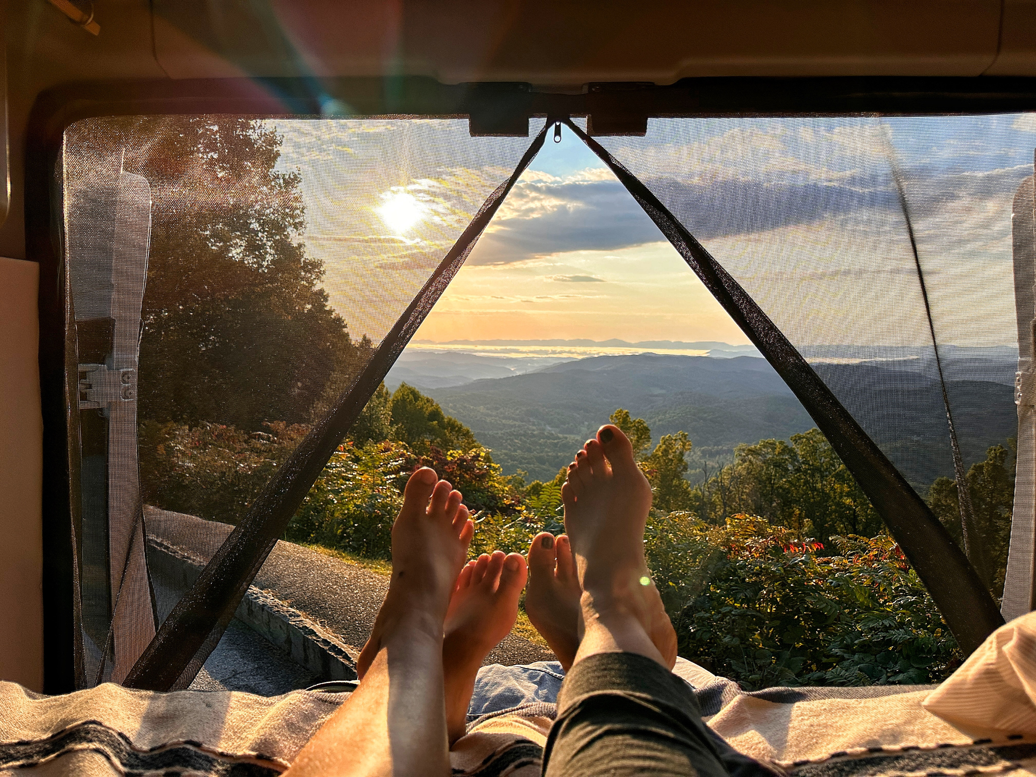 An RV rental offers this peaceful moment: feet propped up, enjoying a vibrant mountain sunset through a bug net.. Winnebago Solis 2022