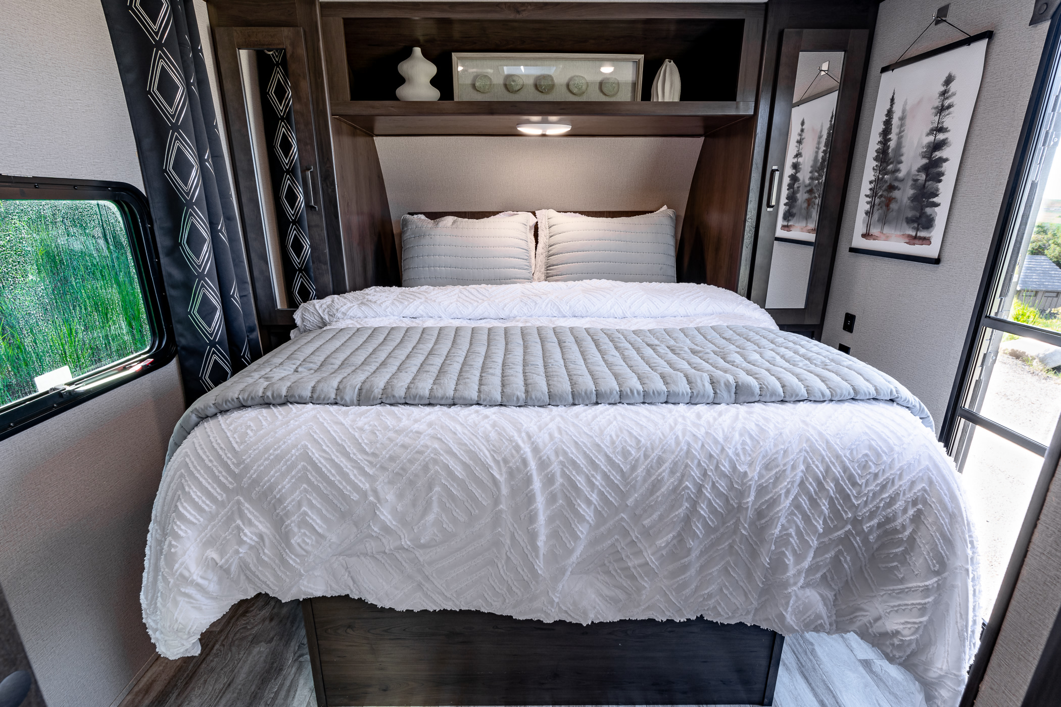 Discover comfort in this RV rental bedroom. Enjoy a plush bed, stylish decor, and refreshing outdoor views from the window.. Grand Design Transcend Xplor 2021