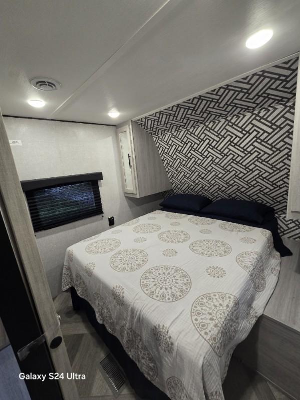 This RV rental bedroom features a comfy bed with patterned blanket, built-in storage, and a large window.. Crossroads RV Zinger Lite 2023