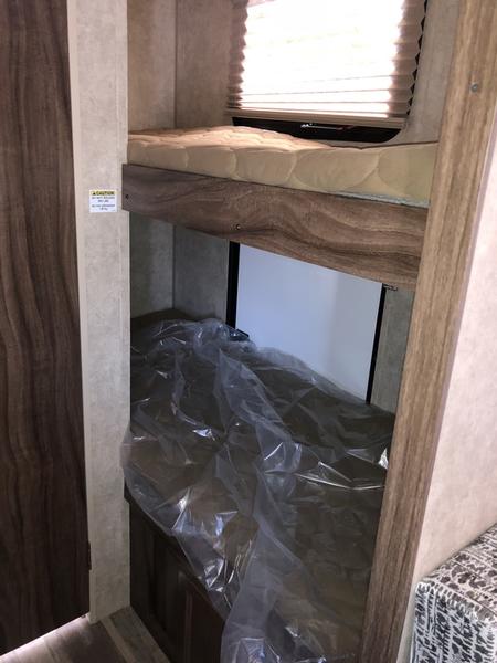 RV rental interior features bunk beds. Top bed mattress exposed, bottom covered in plastic. Window with blinds above.. Forest River Viking 2019