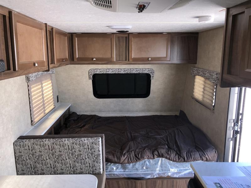 Inside an RV rental: view of a comfy bed with brown bedding and a patterned dinette area. Overhead cabinets complete the space.. Forest River Viking 2019