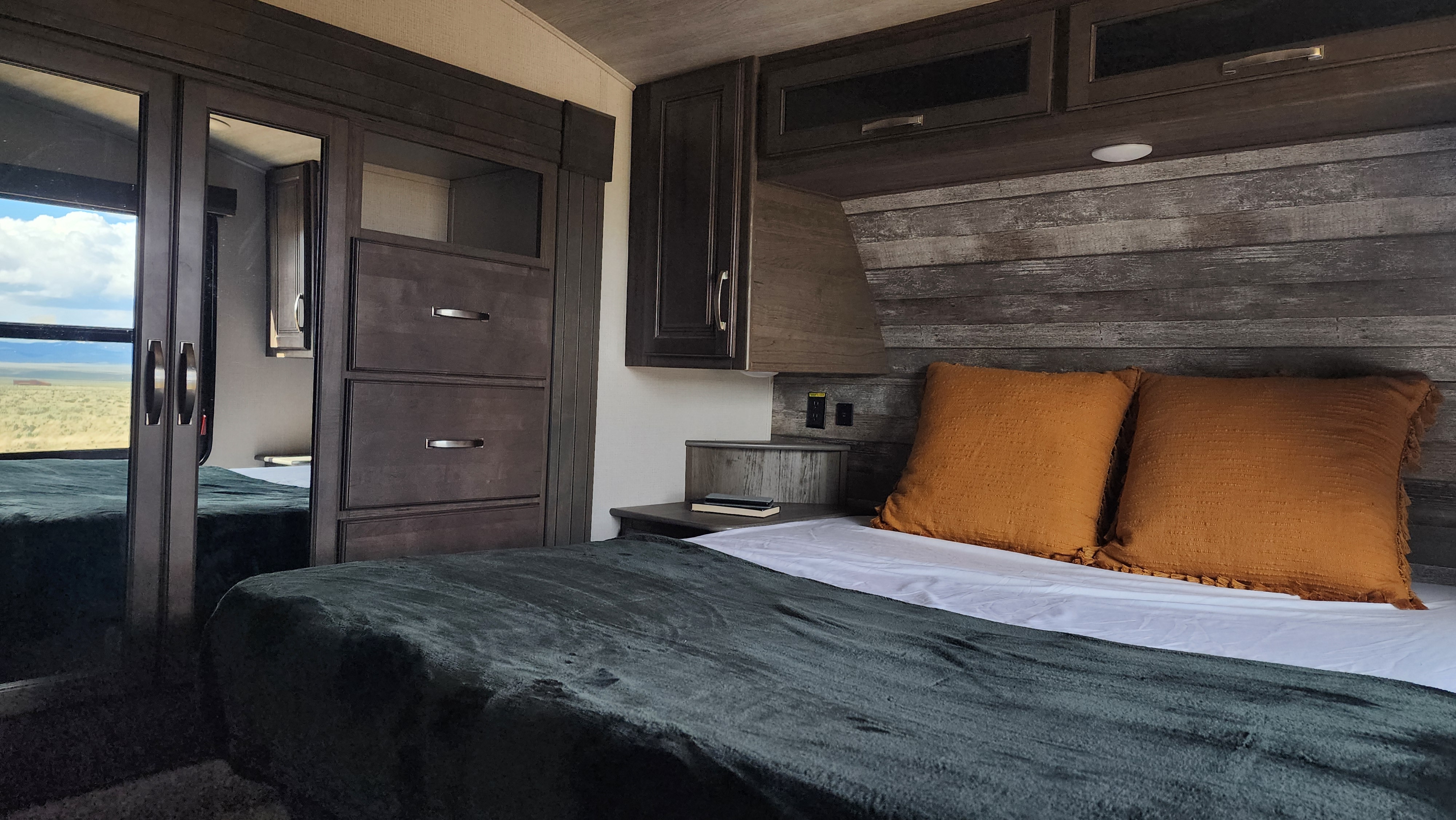 Cozy RV rental bedroom with modern dark wood accents, comfortable bed, and a mirrored wardrobe reflecting a desert view.. Keystone RV Cougar 2023