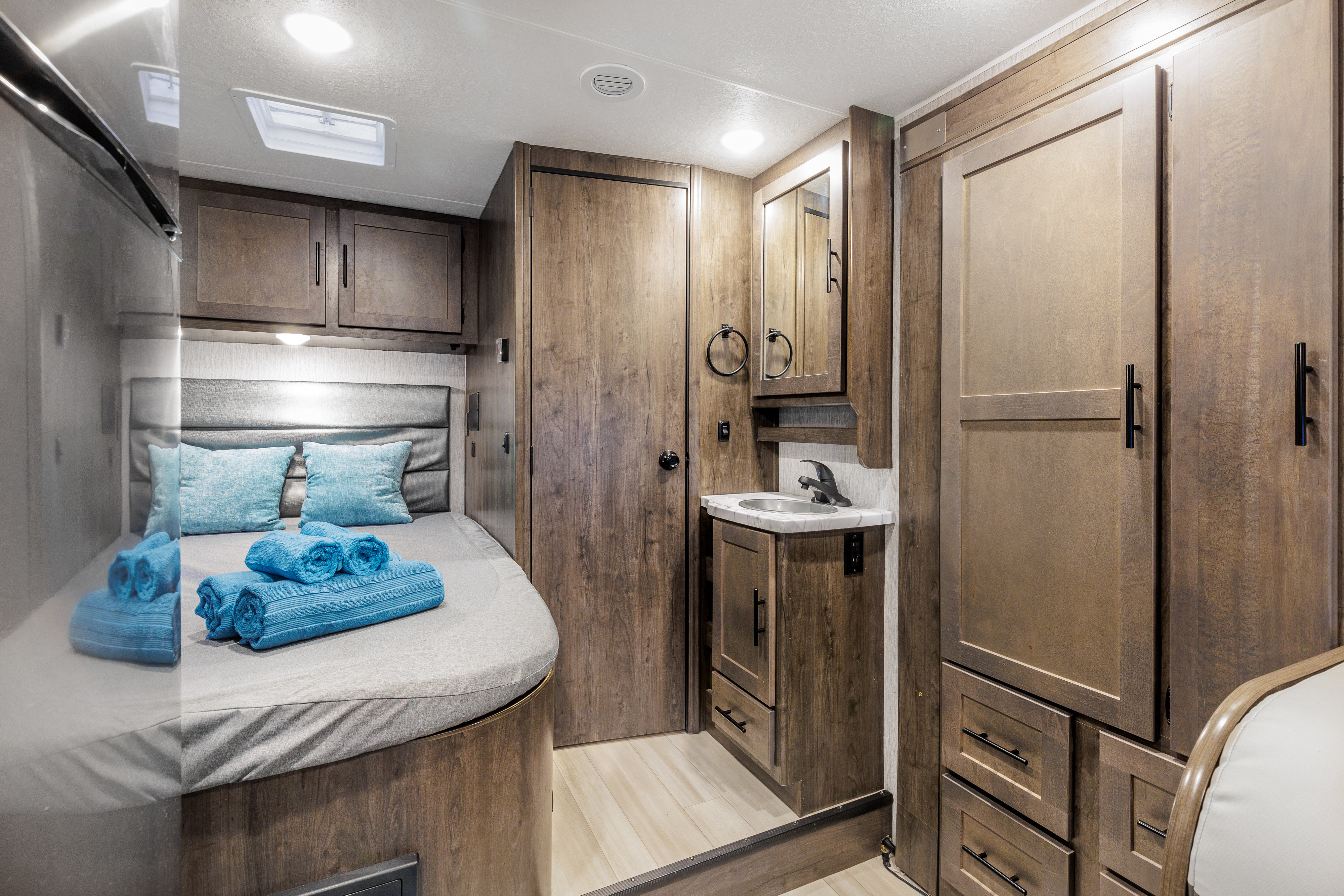 Comfortable RV rental interior showcasing a cozy bedroom with blue towels and a functional bathroom vanity. Perfect for trips.. Coachmen Prism 2024