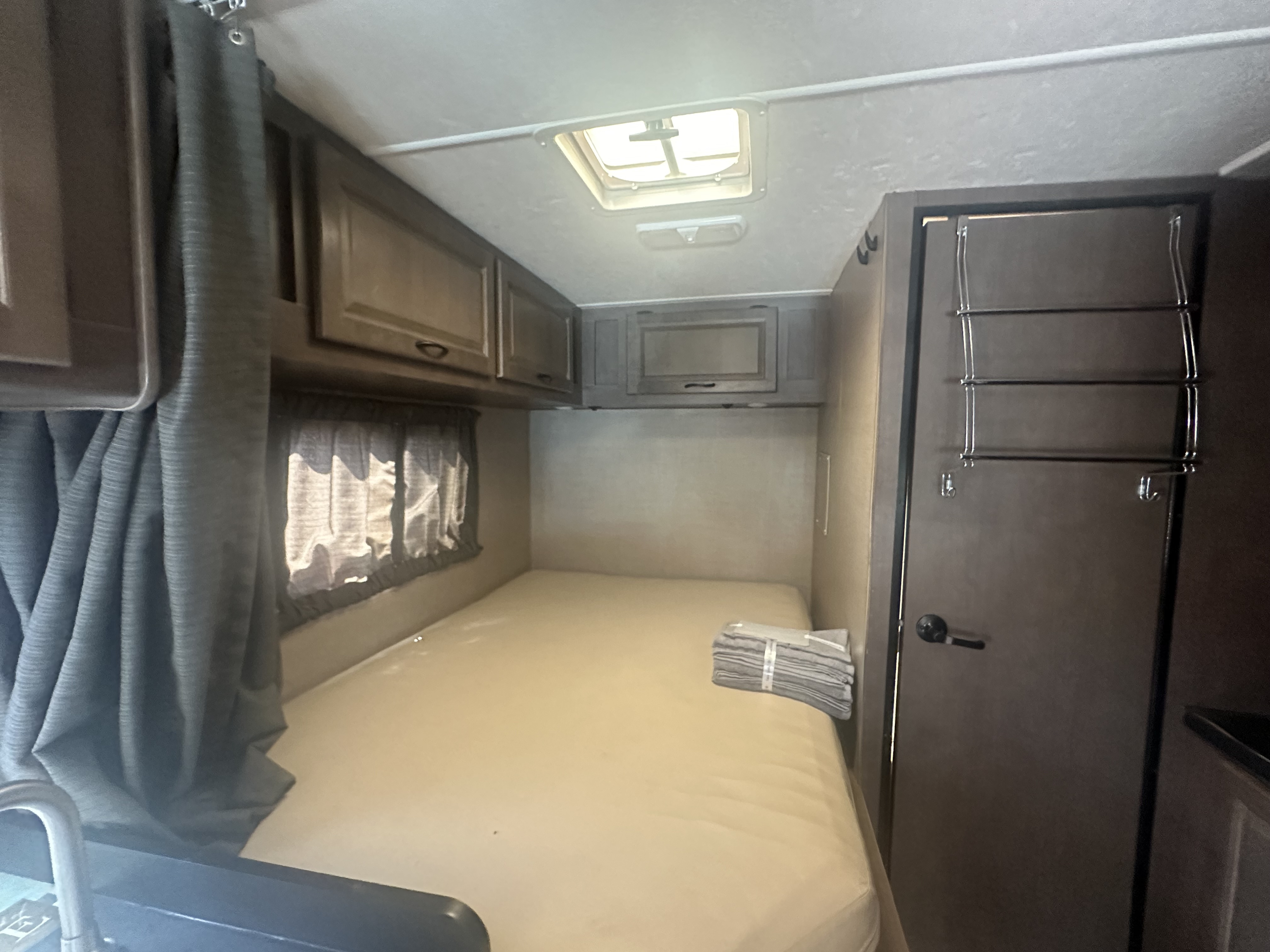 RV rental interior: A bright bedroom with a large bed, overhead storage, a window, and a ceiling vent.. Thor Majestic 2017