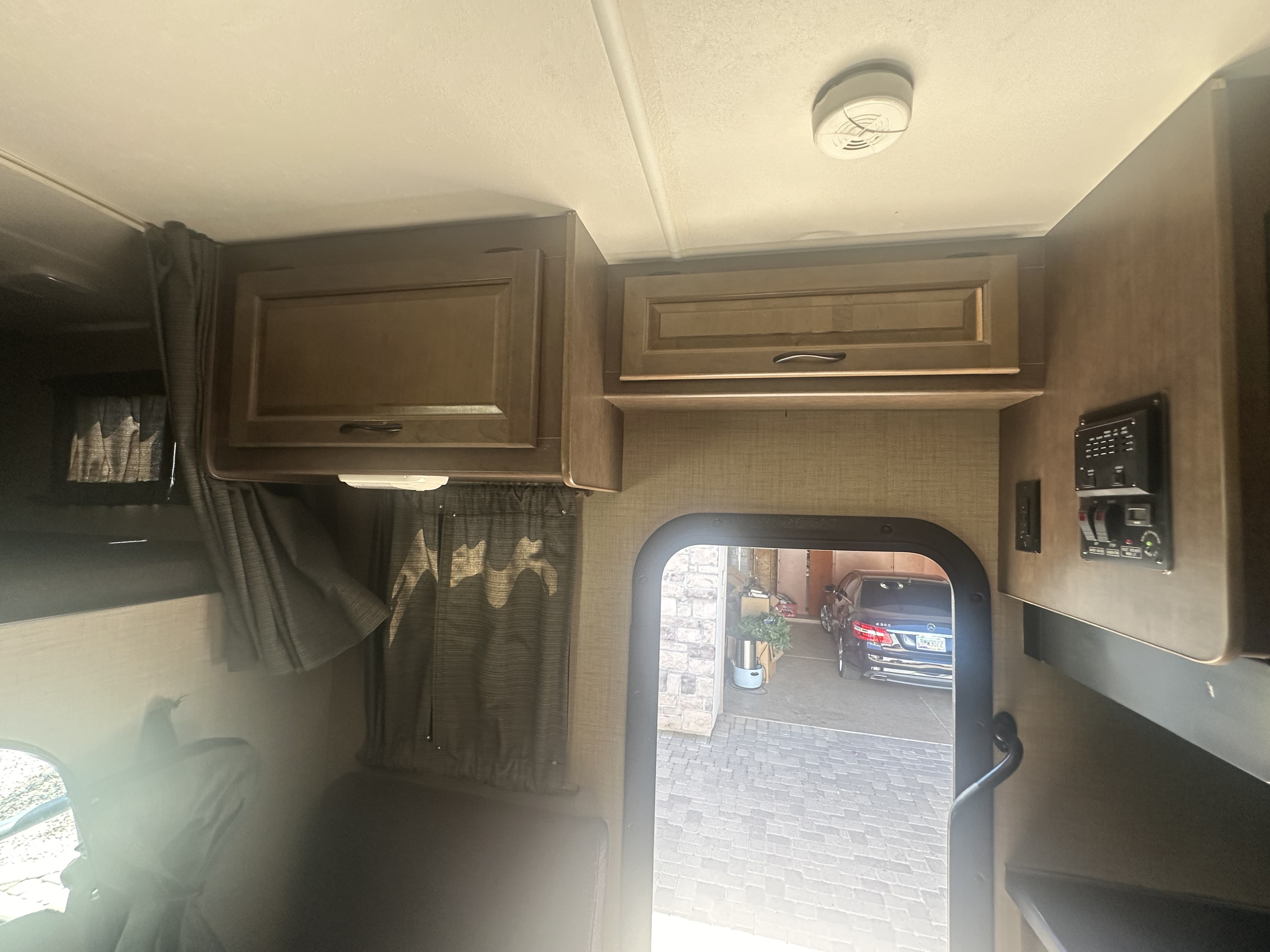 The interior of an RV rental features wood cabinets, a smoke detector, control panel, and a car seen through the door.. Thor Majestic 2017
