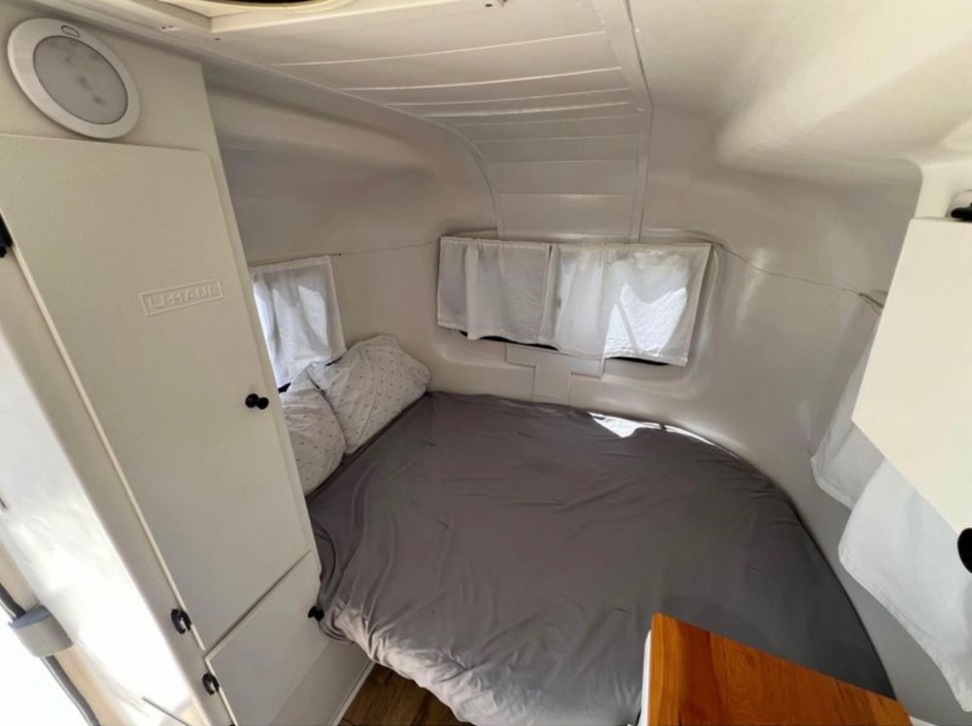 U-Haul RV rental interior showing a compact, white-walled sleeping area with a gray bed, windows, and storage.. Burro Fiberglass CT13 Camper 1986