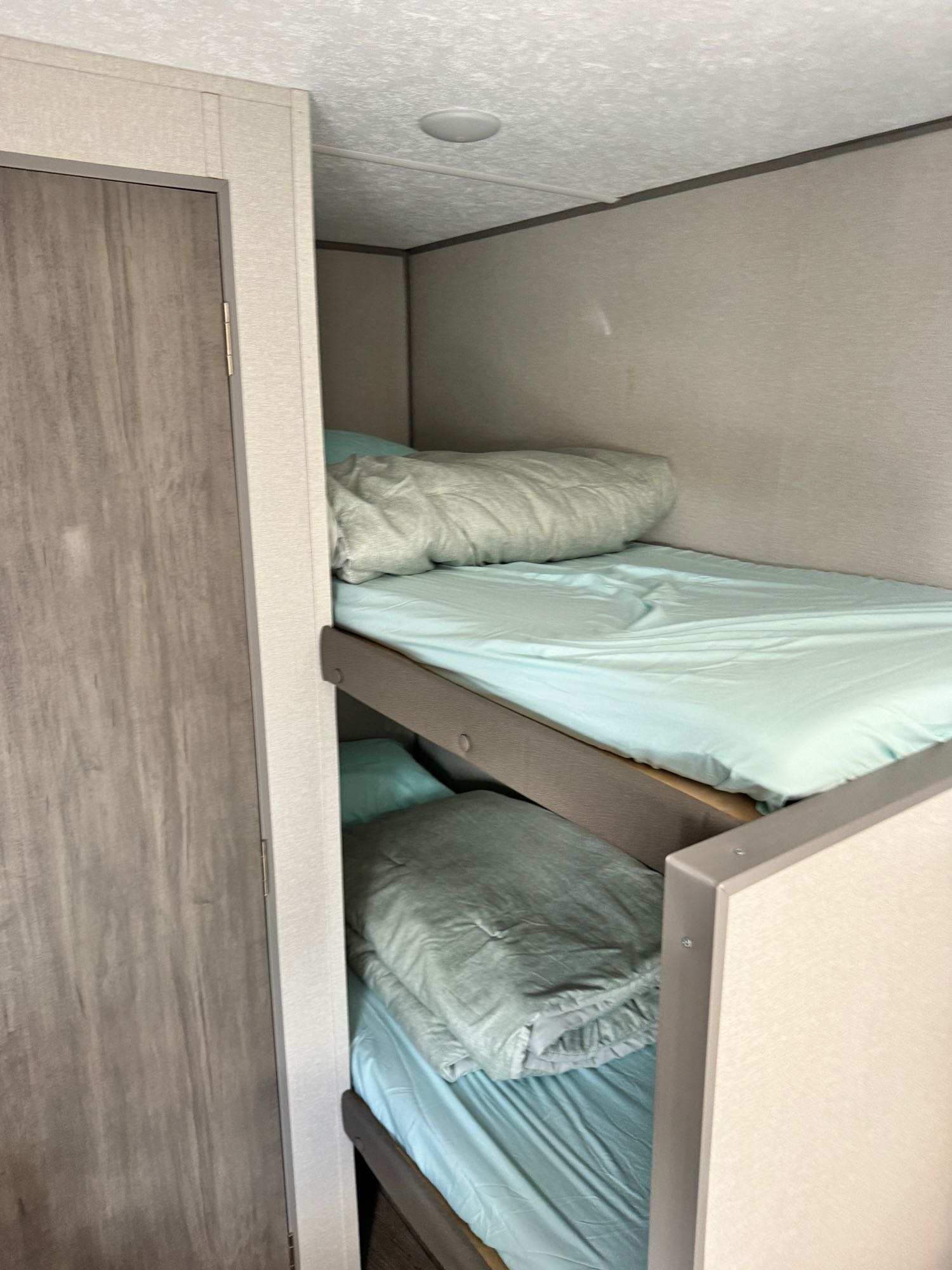 Cozy RV rental interior features bunk beds with light blue bedding, perfect for travel, next to a wood-grain door.. Coachmen Catalina Summit 164BHX 2024