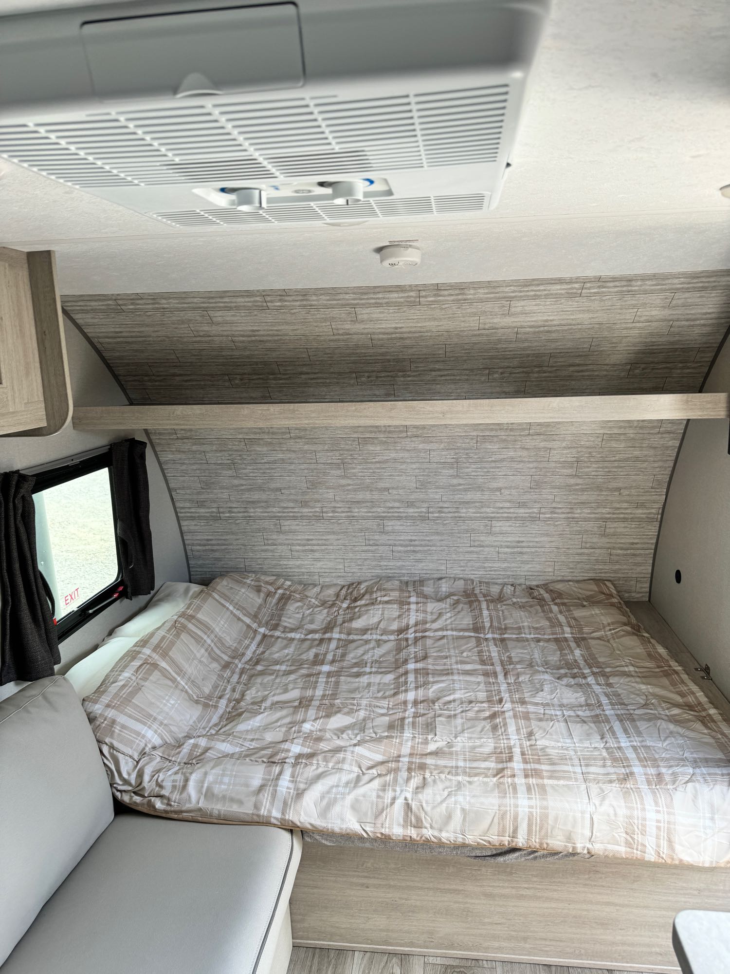 Inside a modern RV rental: a cozy bedroom with a plaid comforter, overhead AC unit, and a convenient exit window.. Coachmen Catalina Summit 164BHX 2024