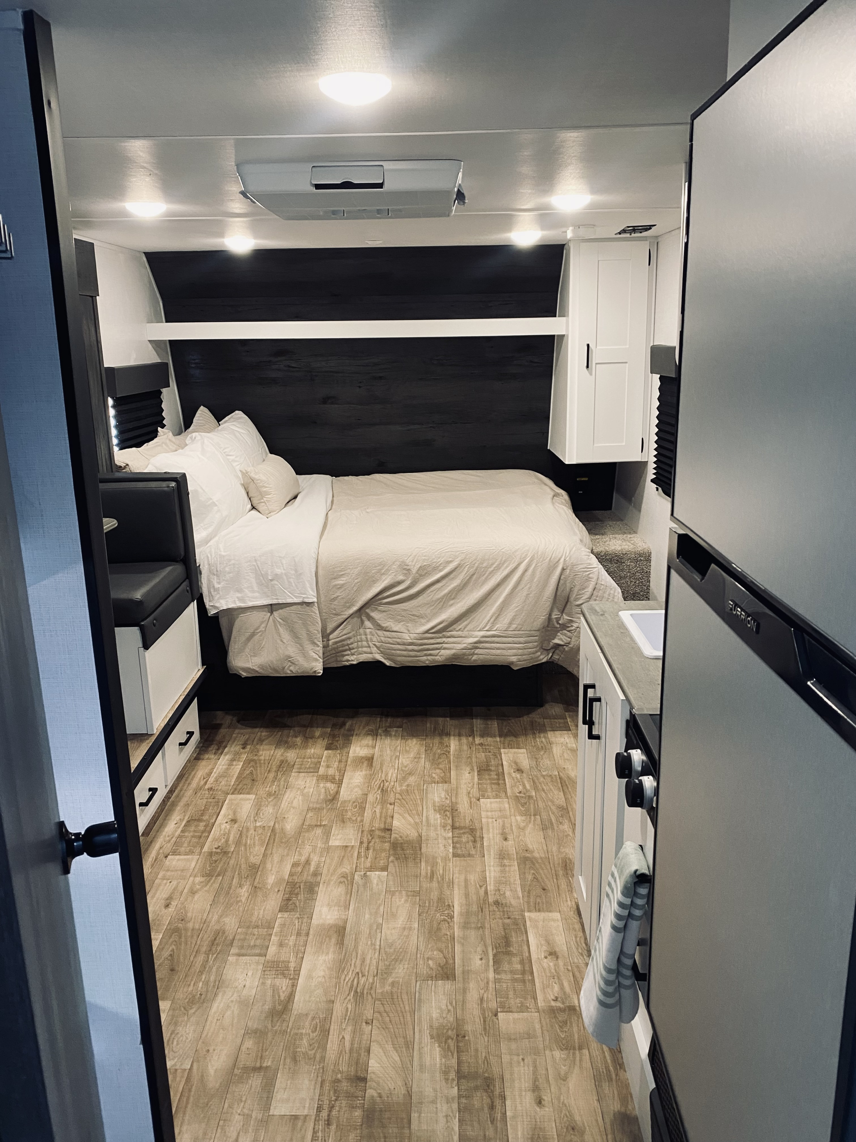 Cozy RV rental interior with a bedroom, compact kitchen, and dining nook, featuring wood-look flooring and bright lighting.. Keystone RV Hideout 2023
