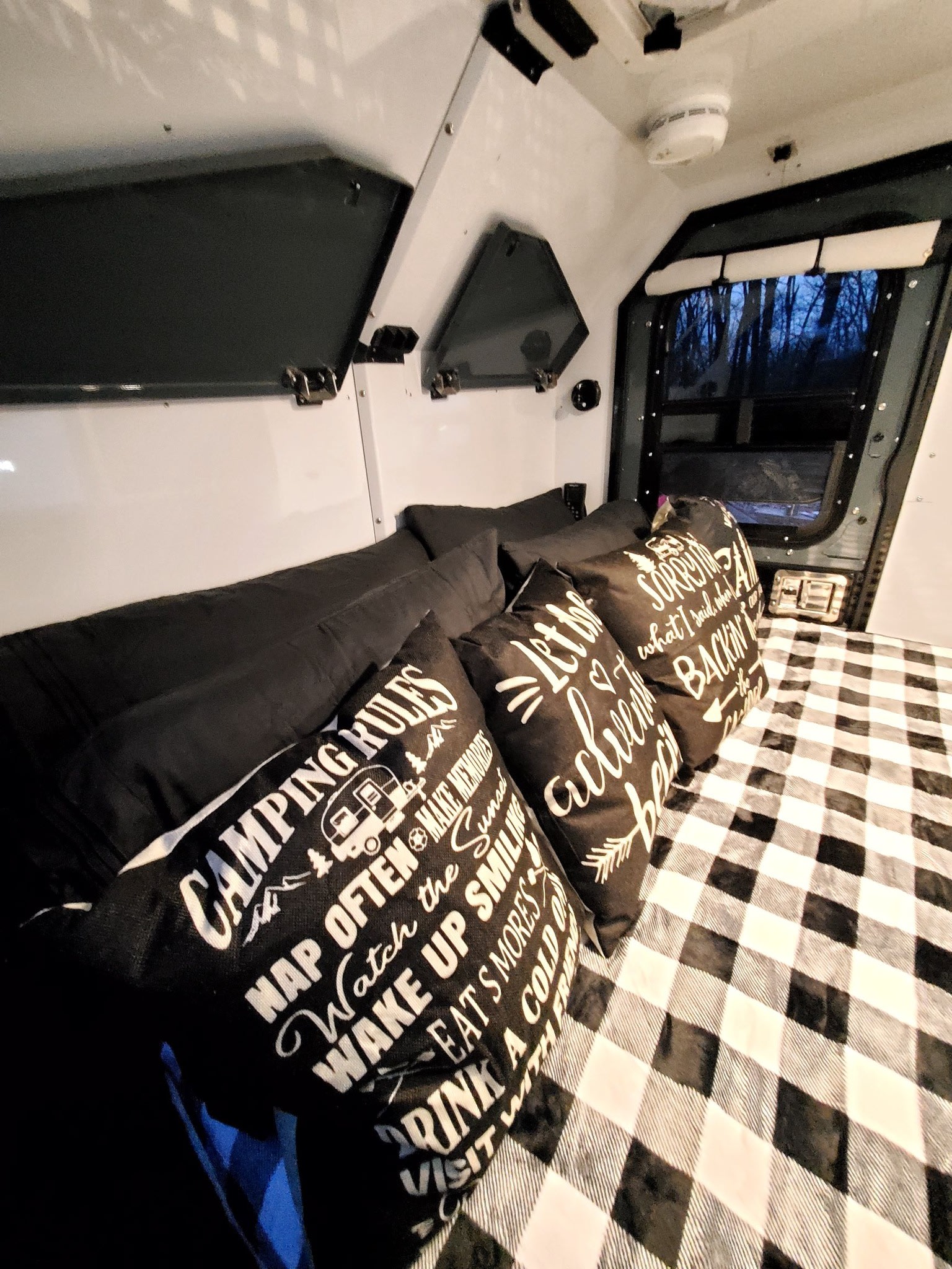 Cozy RV rental interior with comfy bed, buffalo check blanket, and fun camping pillows.. Off Grid Trailers Off Grid Trailers Trailer 2021