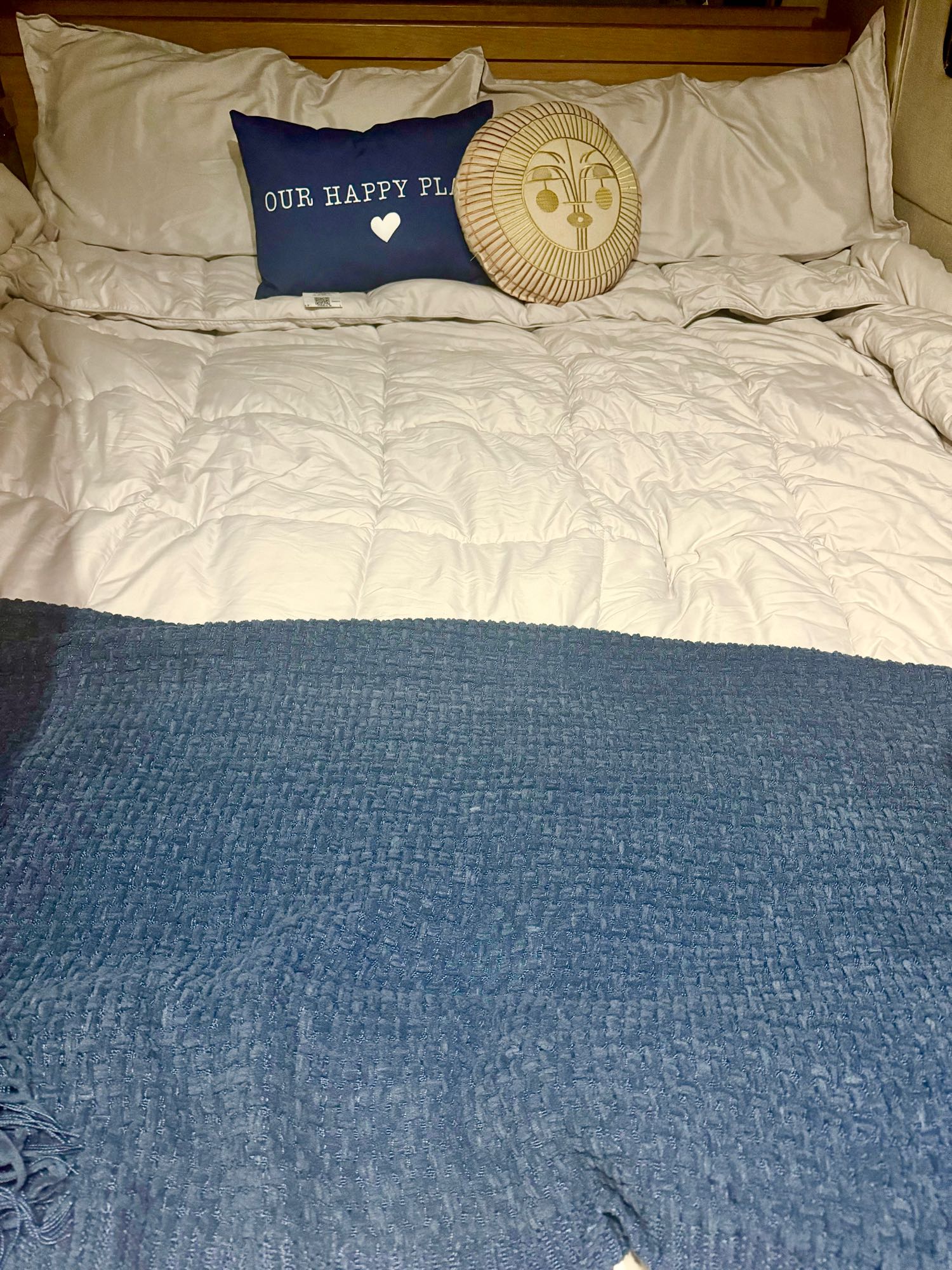 Cozy bed setup in an RV rental, featuring a blue blanket, white comforter, and "Our Happy Place" pillow.. Roadtrek Adventurous XL 2017