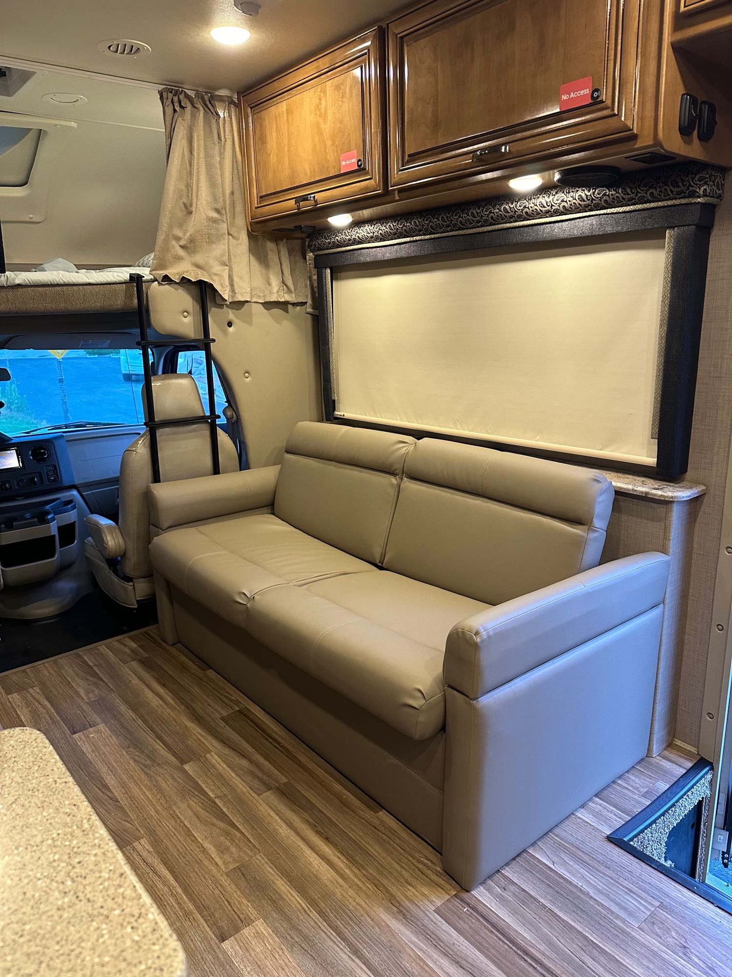 Inside a well-appointed RV rental: light-colored sofa, overhead bunk, and front cabin area. Perfect for road trips.. Thor Quantum 2017