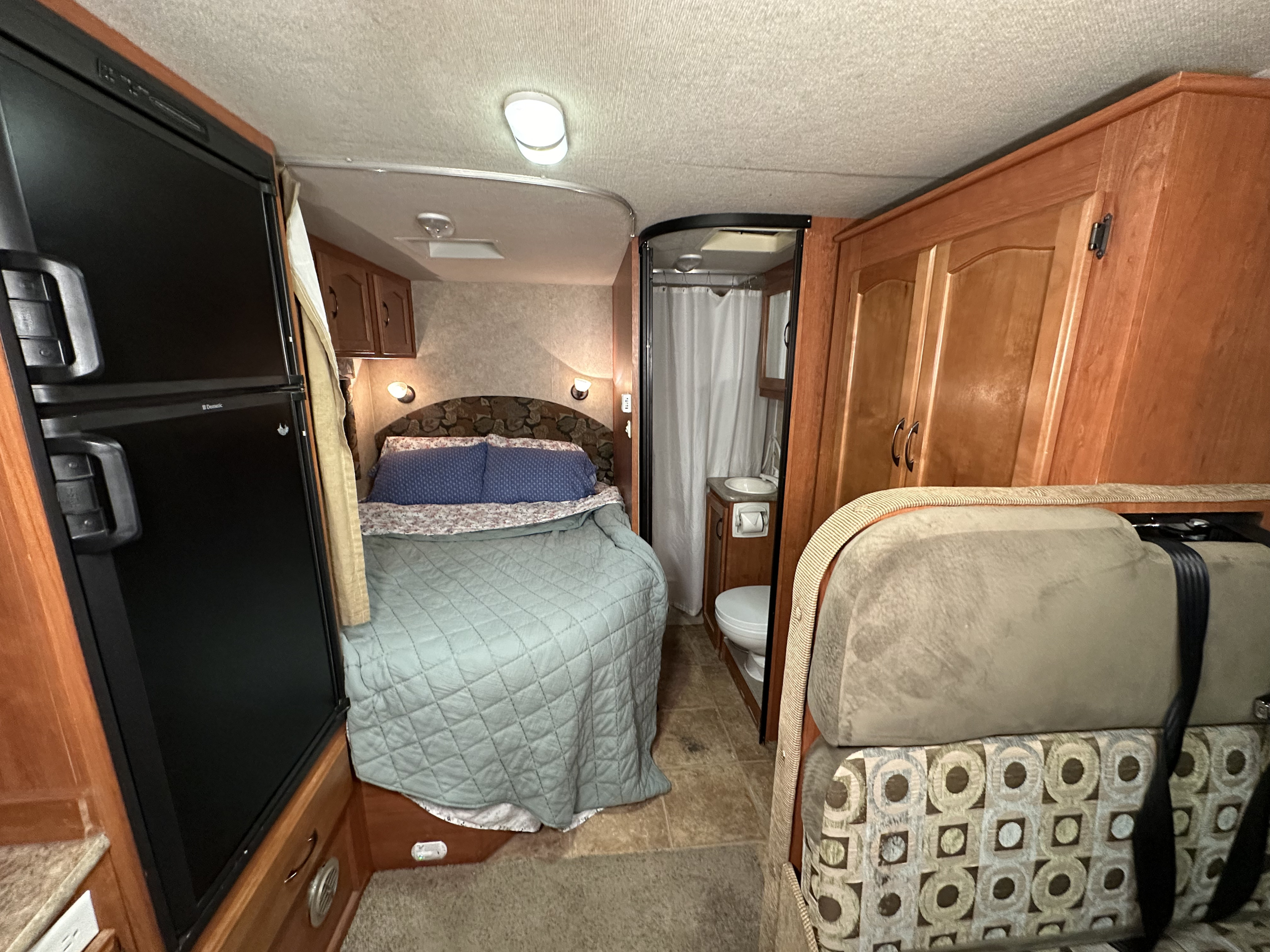 Cozy RV rental interior featuring a bed, compact bathroom, and large refrigerator. Perfect for travel adventures.. Adventurer Adventurer Motorhome 2013